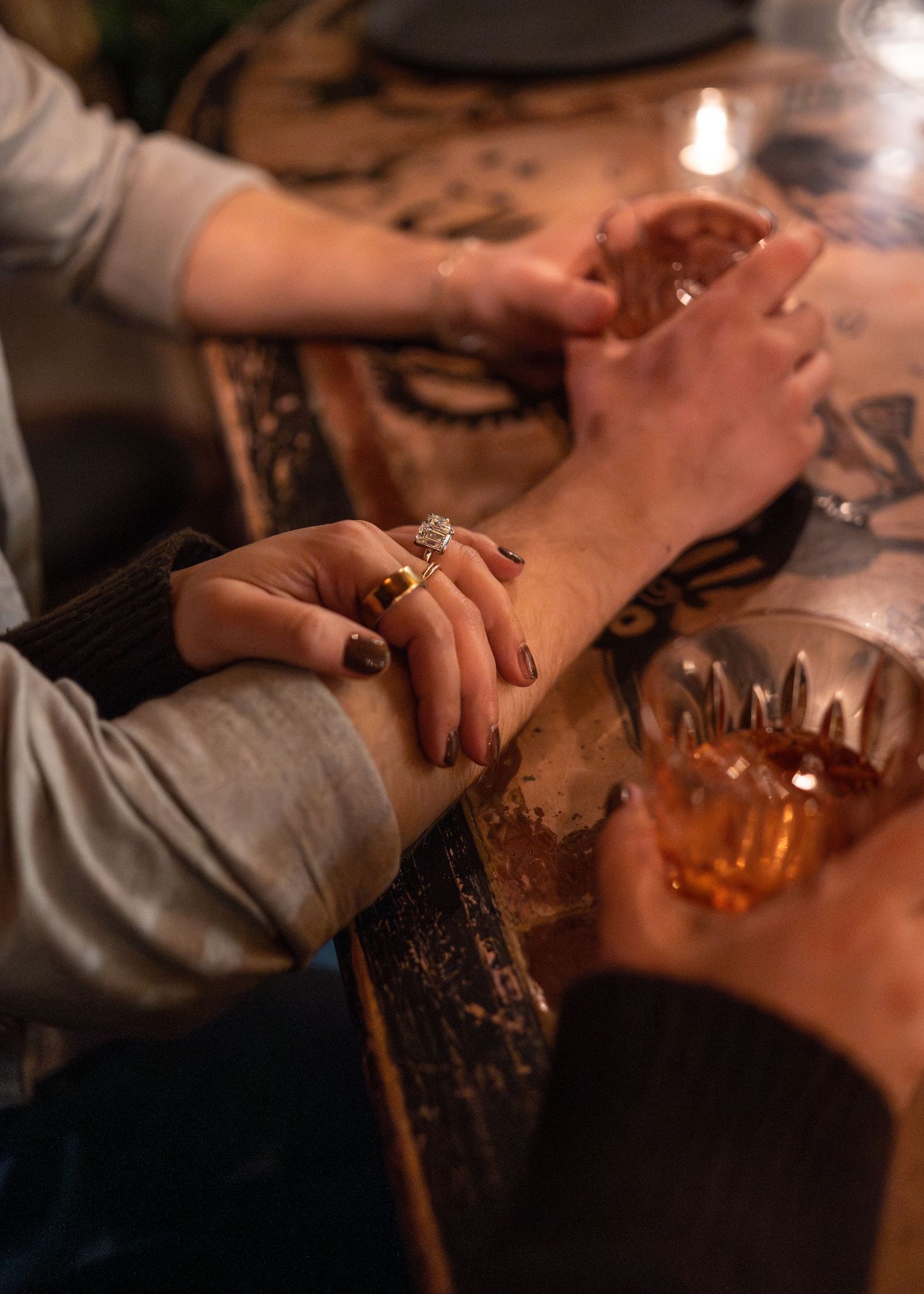 Close-up of hands holding drinks across a wooden bar table in warm lighting.