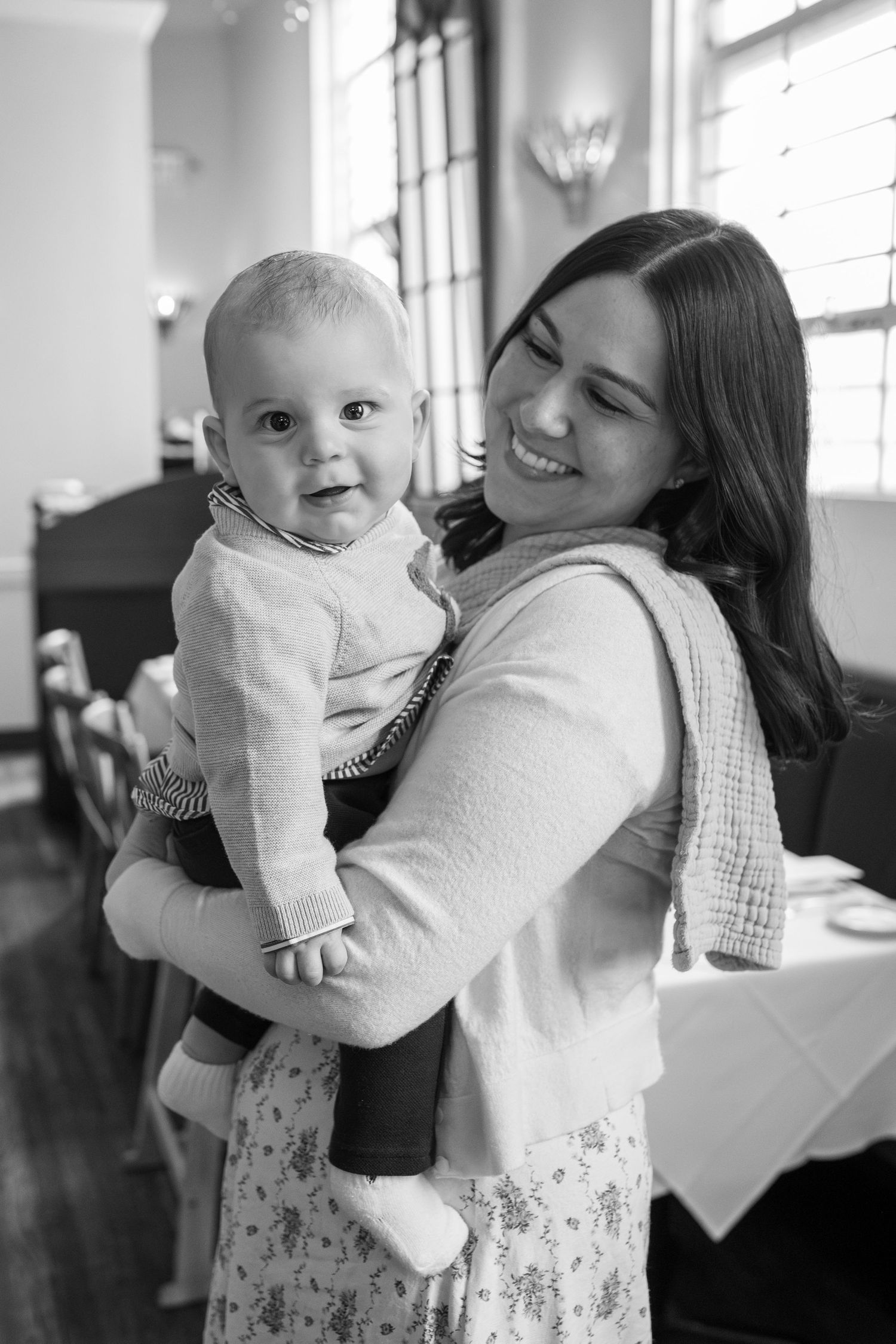 Smiling mother holding happy baby boy in black and white portrait at restaurant.