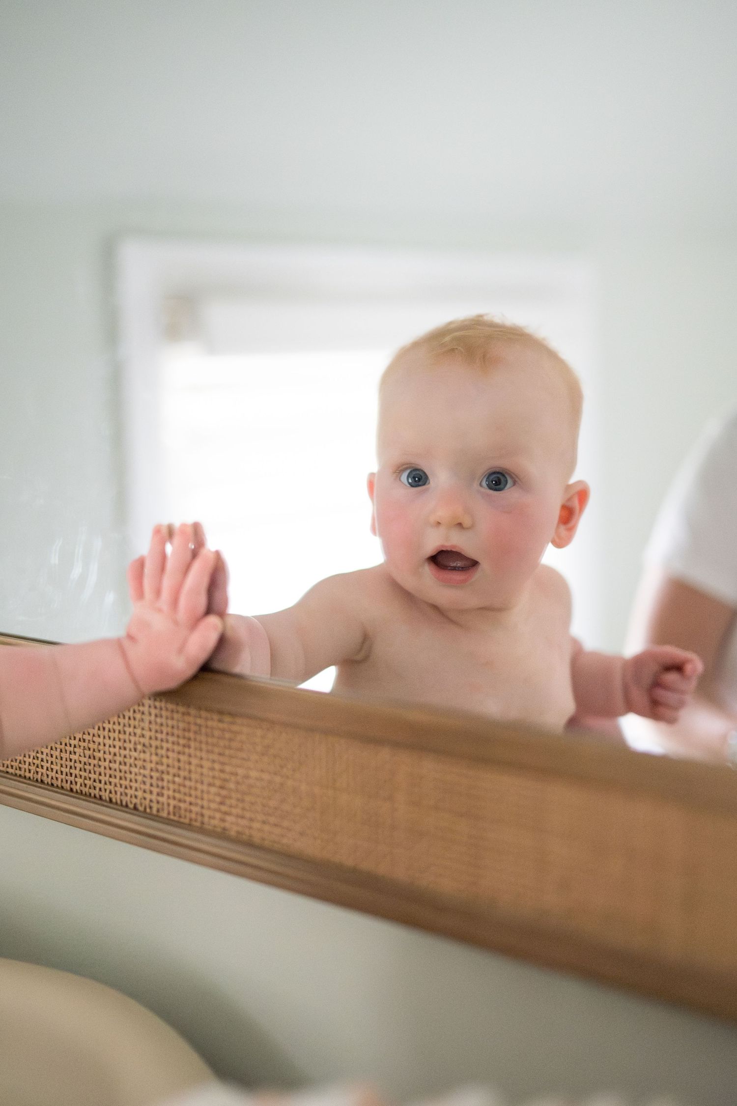 A curious baby reaches toward their reflection in a wooden-framed mirror.