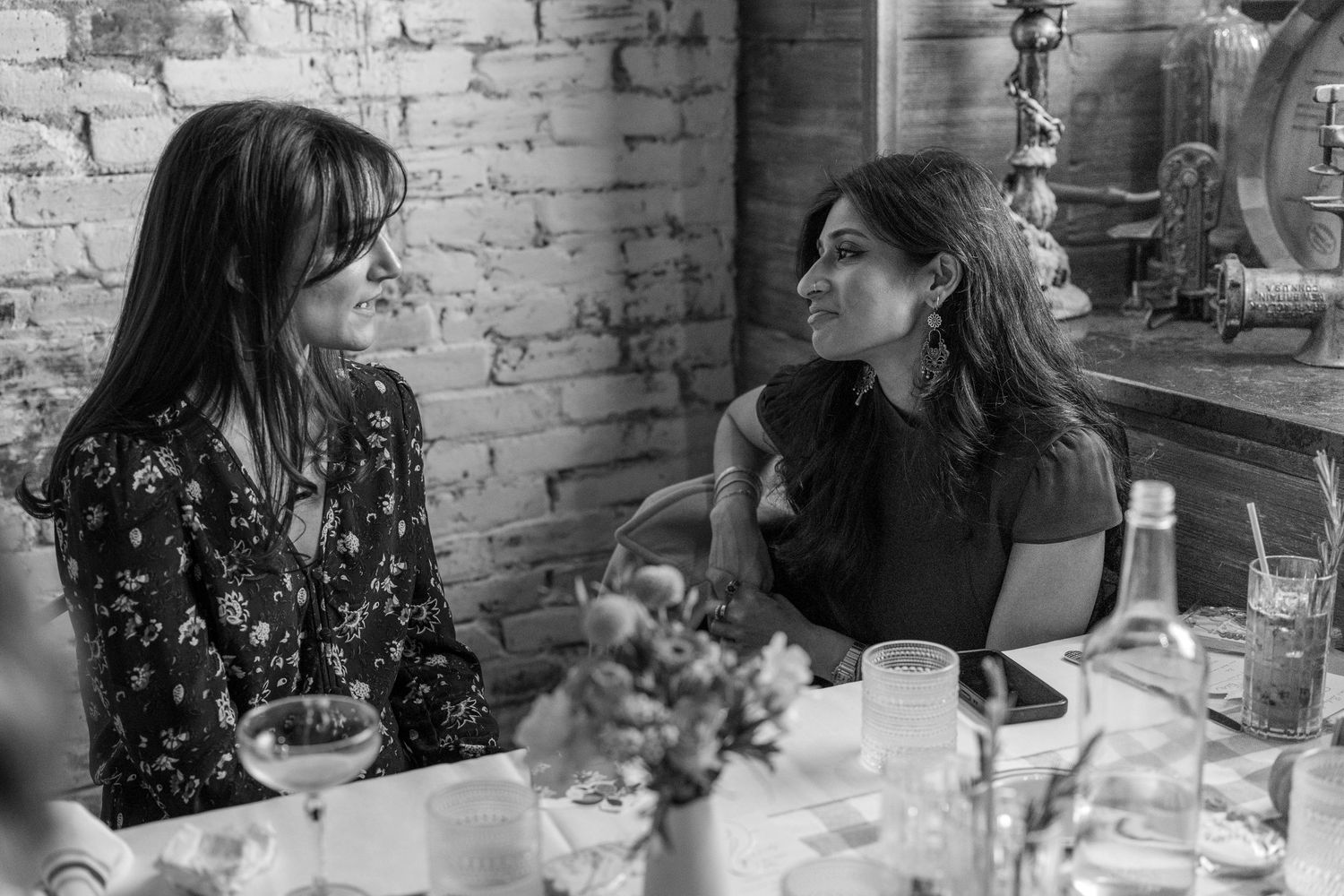 Friends engaged in conversation at a rustic restaurant with exposed brick walls.