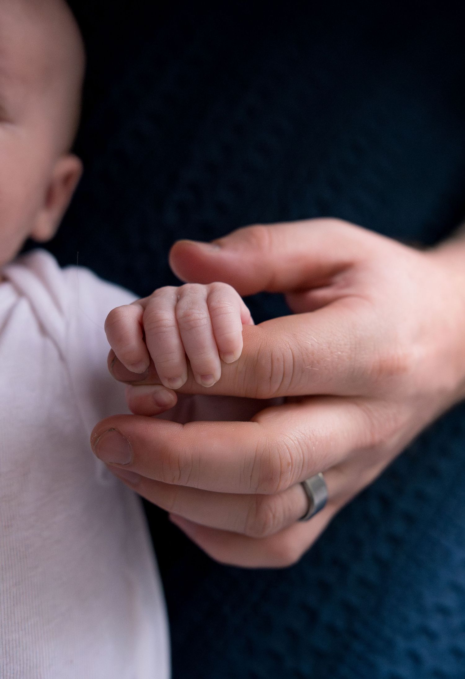 Close-up of small infant hand grasping adult finger against dark background.