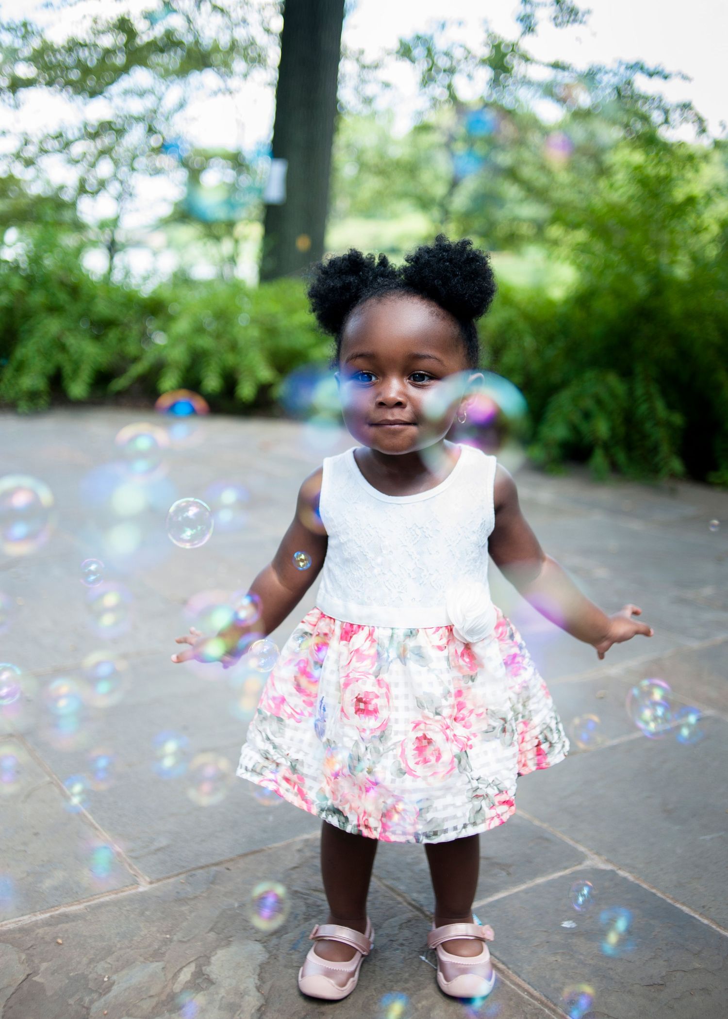 Child in floral dress plays with bubbles outdoors.