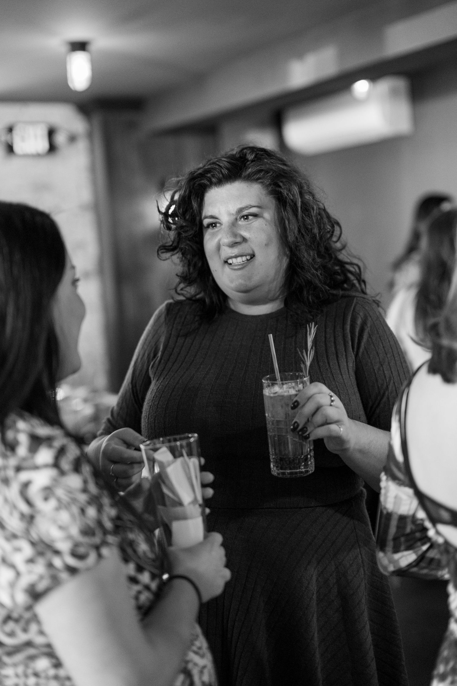 A candid black and white photo of people enjoying drinks and conversation at a social gathering.