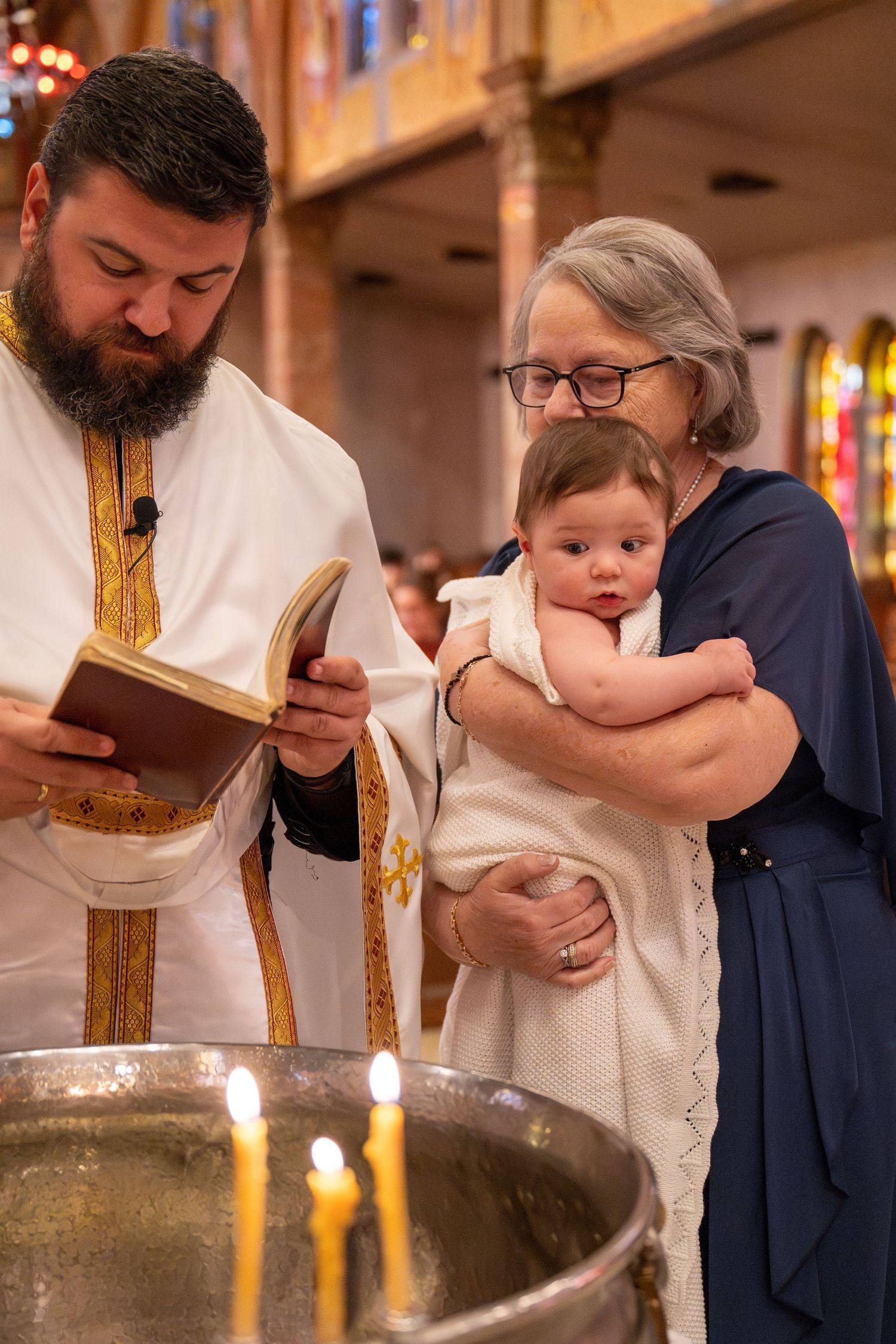 An Orthodox Christian baptism ceremony with lit candles and traditional vestments.