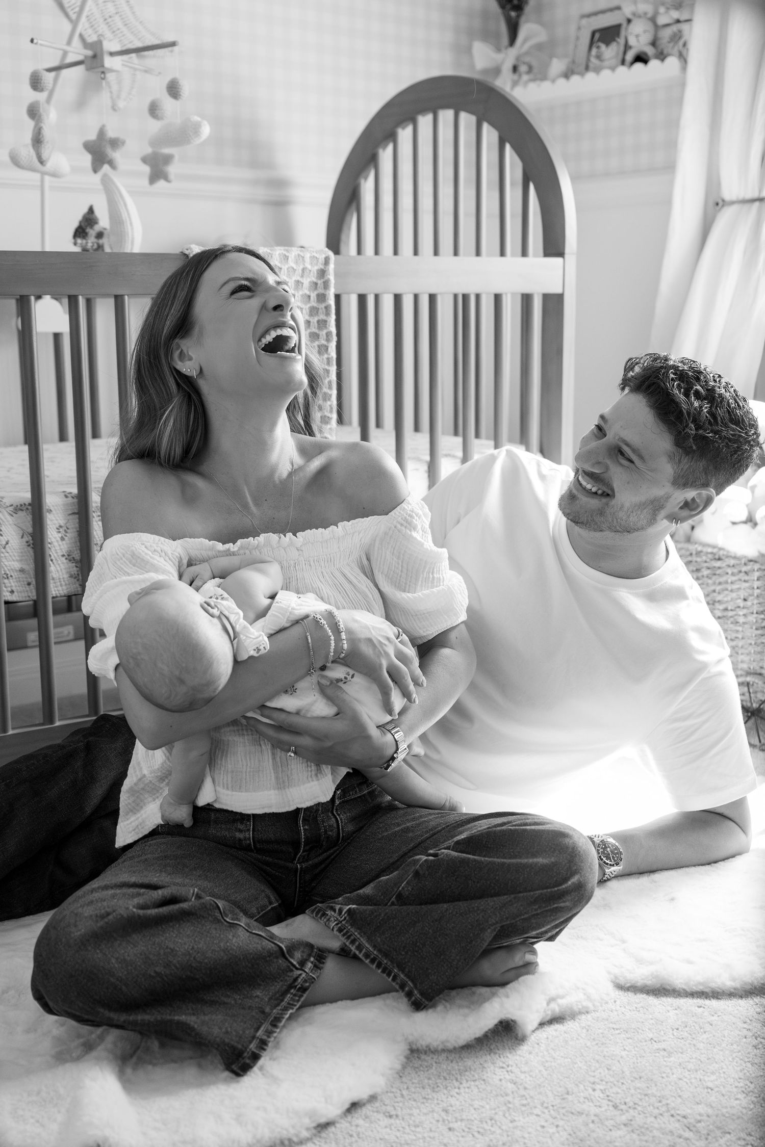 Joyful black and white series of parents sharing laughs while playing with infant on floor.
