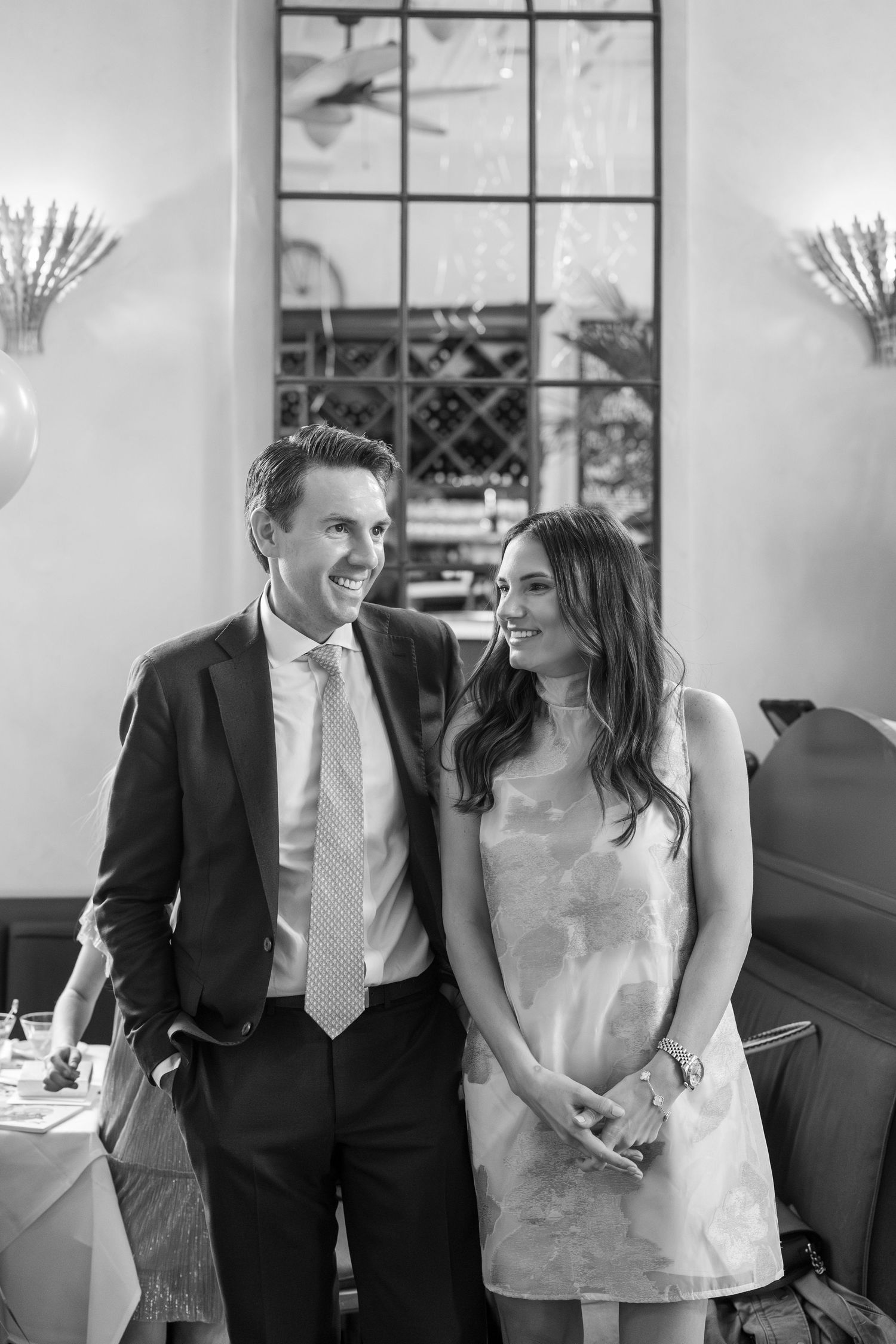 Elegant couple in formal attire smiling together in a stylish restaurant, black and white photo.