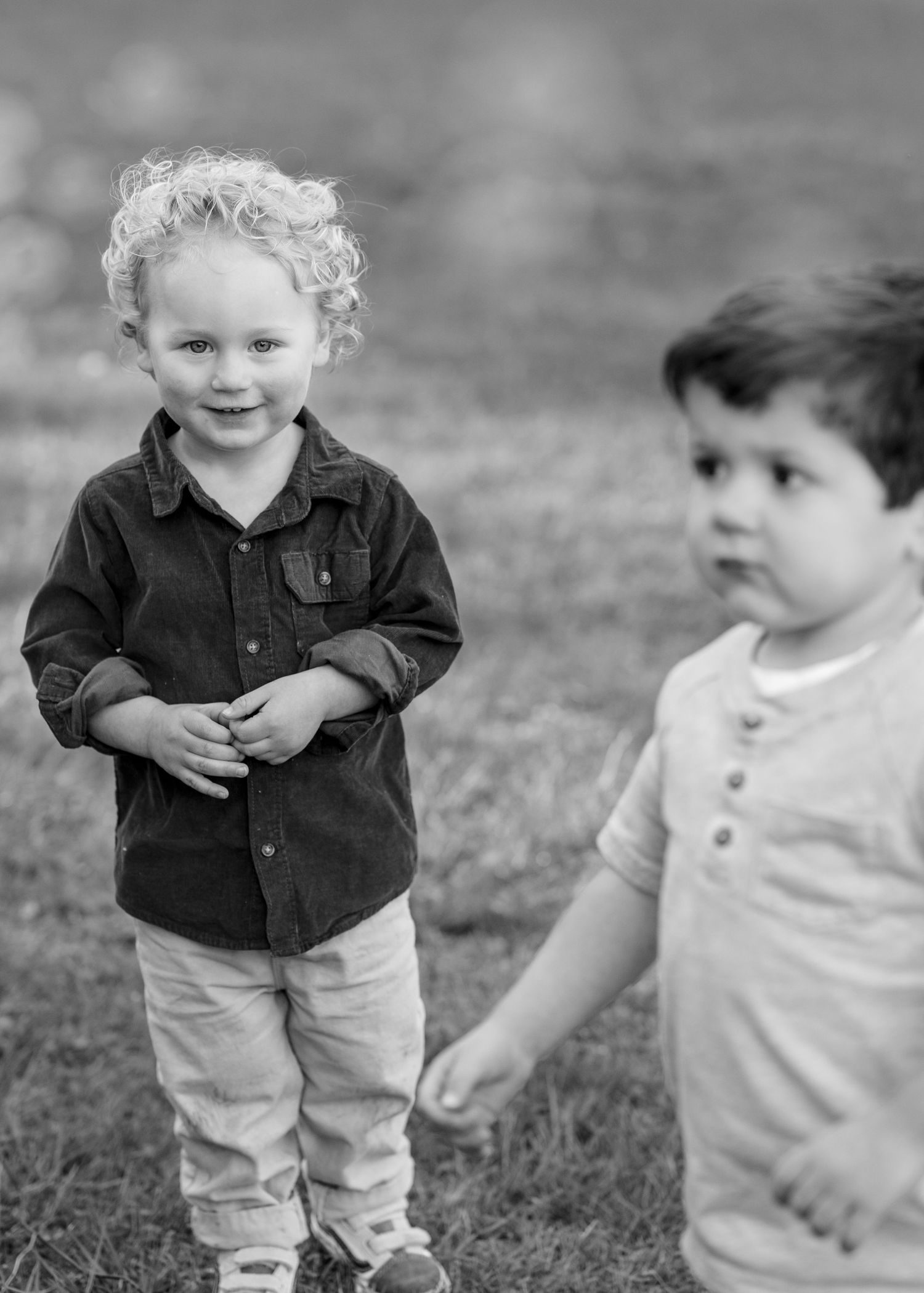 Two young boys stand together on a grassy field in a black and white outdoor portrait photo.