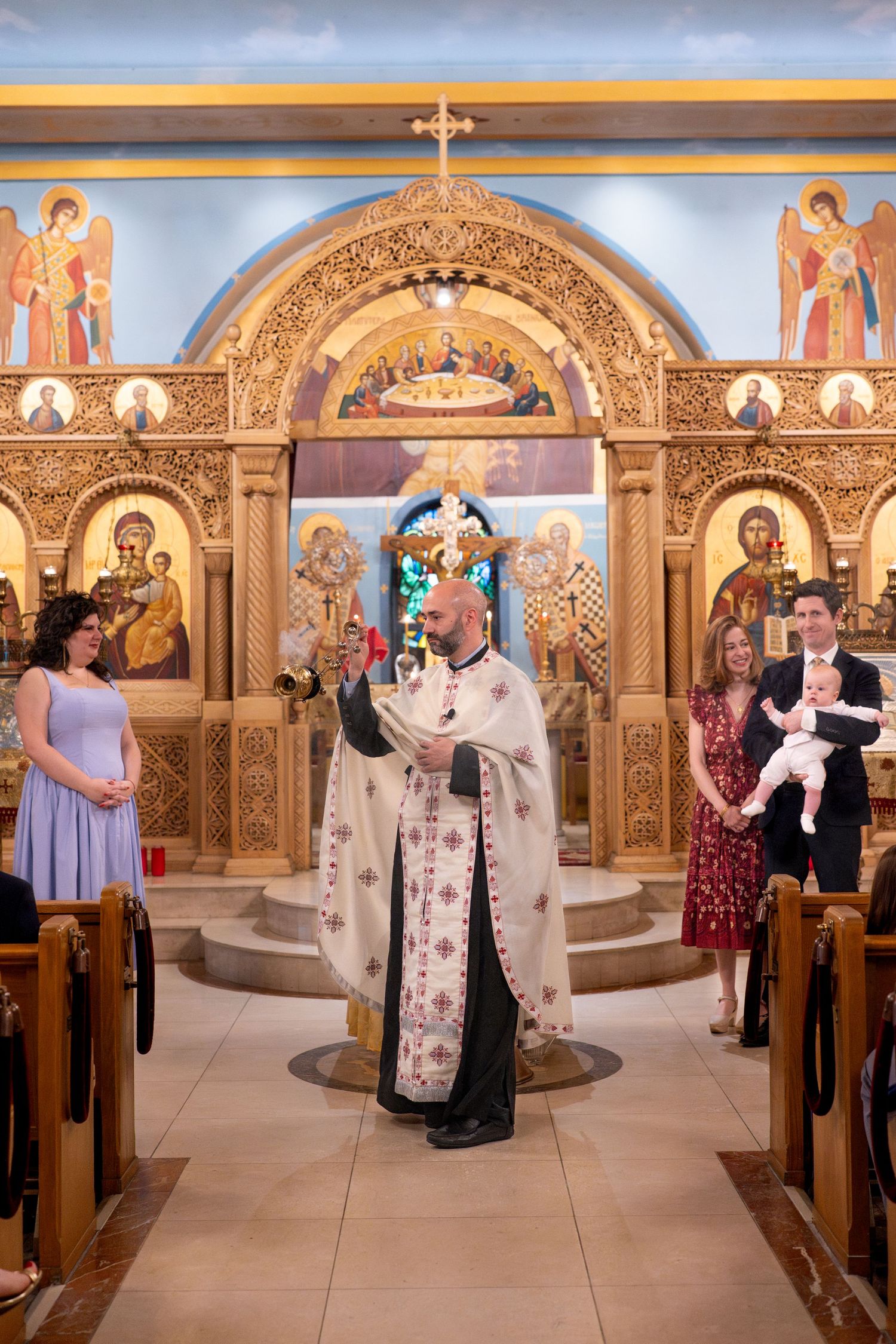 A religious ceremony takes place inside an ornate Orthodox church with golden iconostasis and decorative arches.