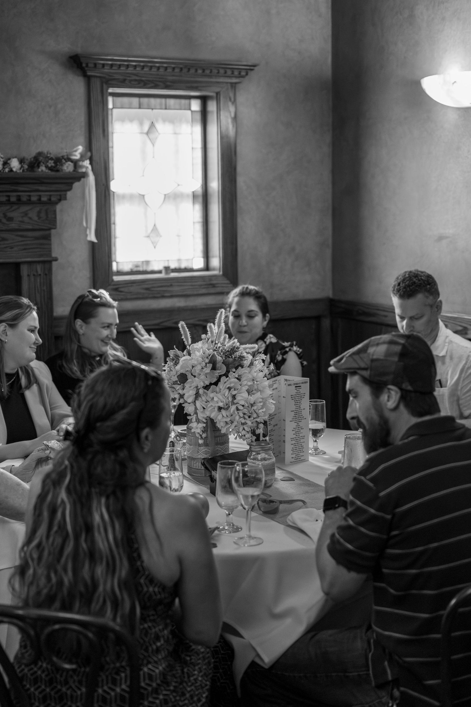 A black and white photo of people dining at a round table with floral centerpiece.
