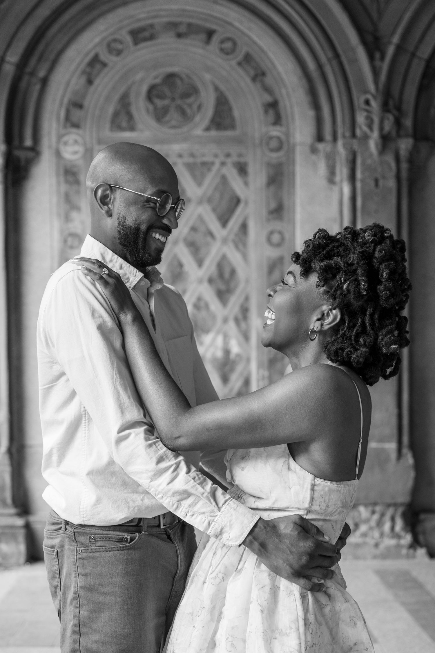 A couple embraces under an ornate archway in a romantic black and white photograph.