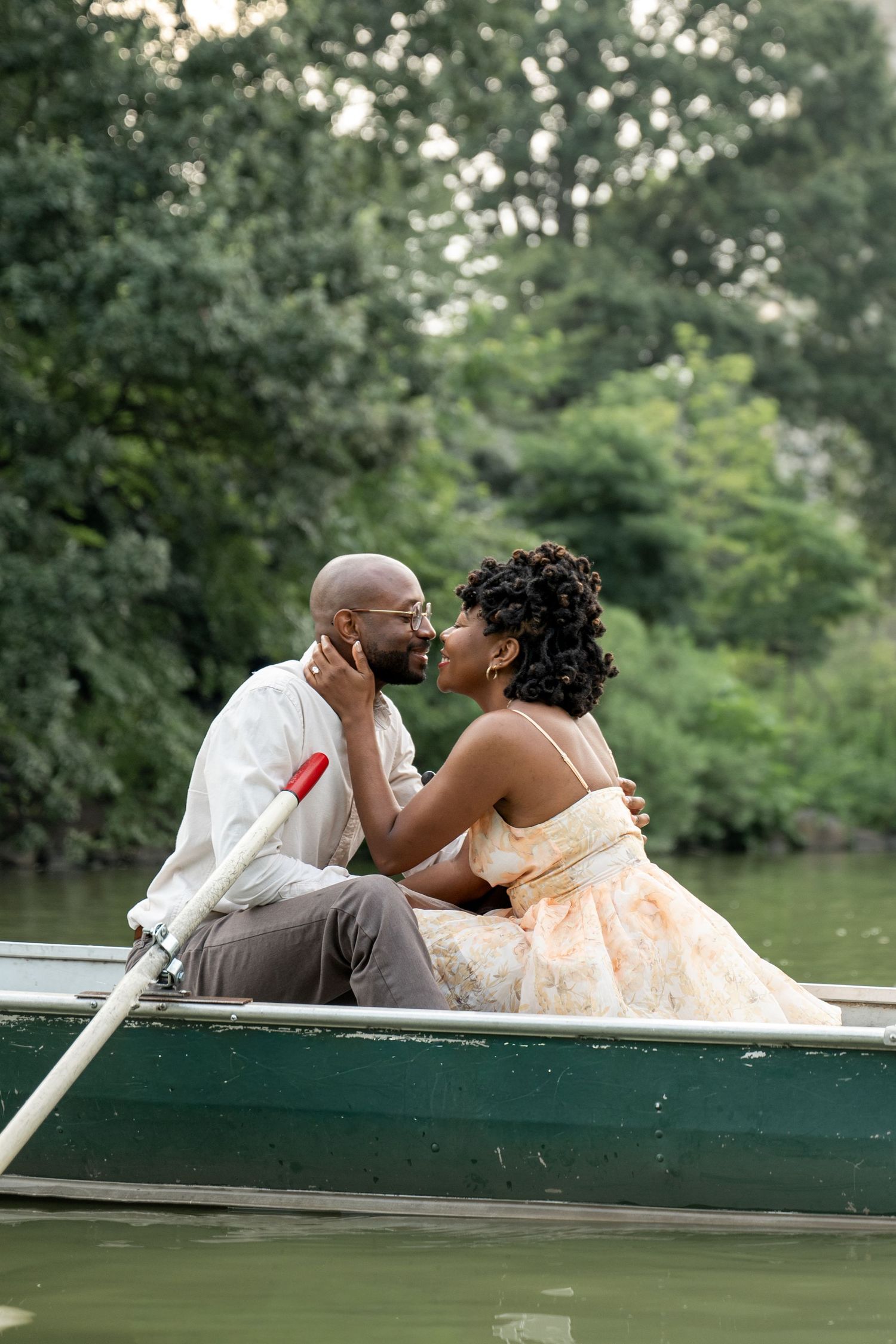 A couple shares an intimate moment while sitting in a rowboat on a peaceful lake.
