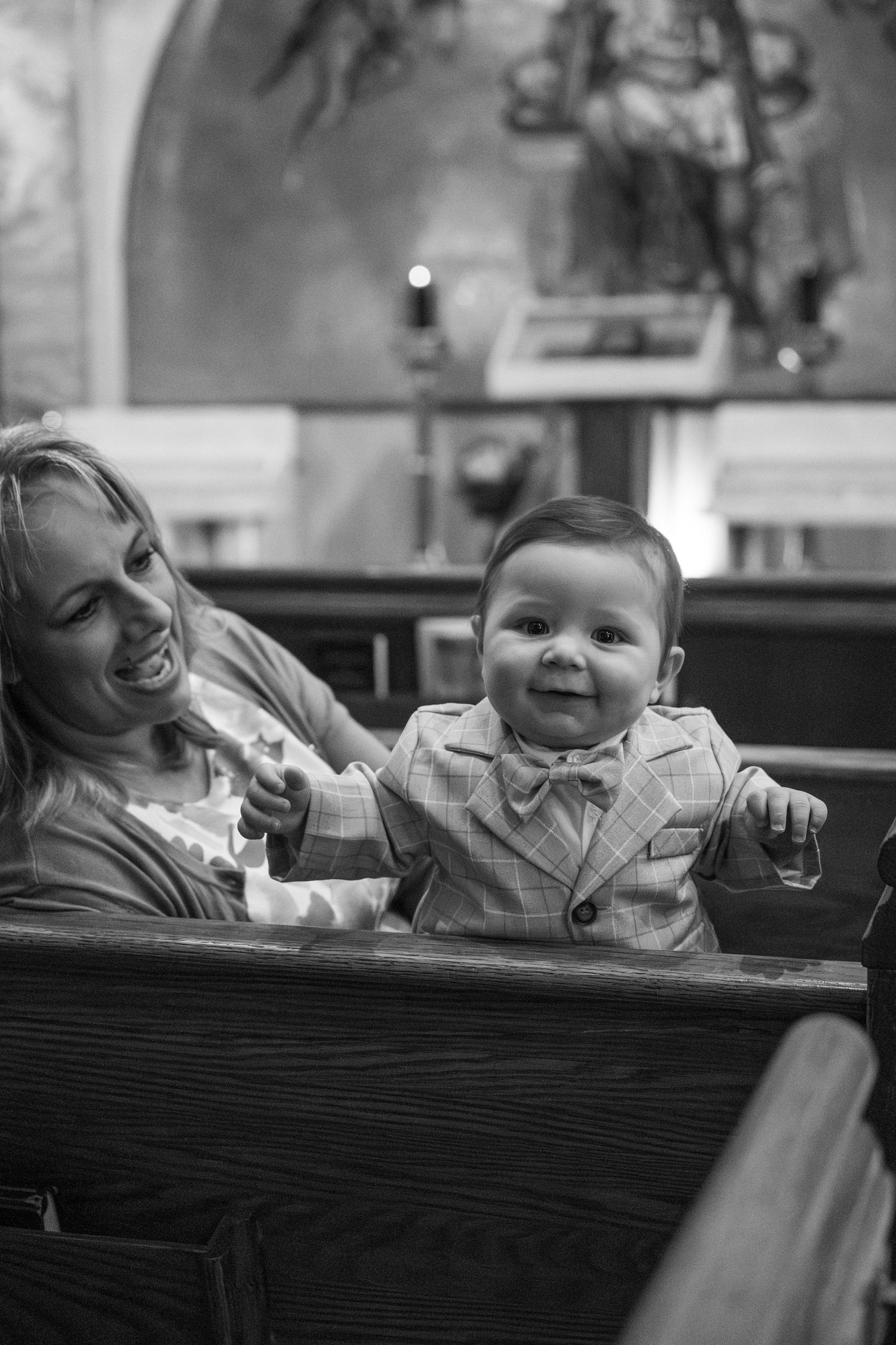 A smiling baby in formal wear sits in a church pew during a special ceremony.