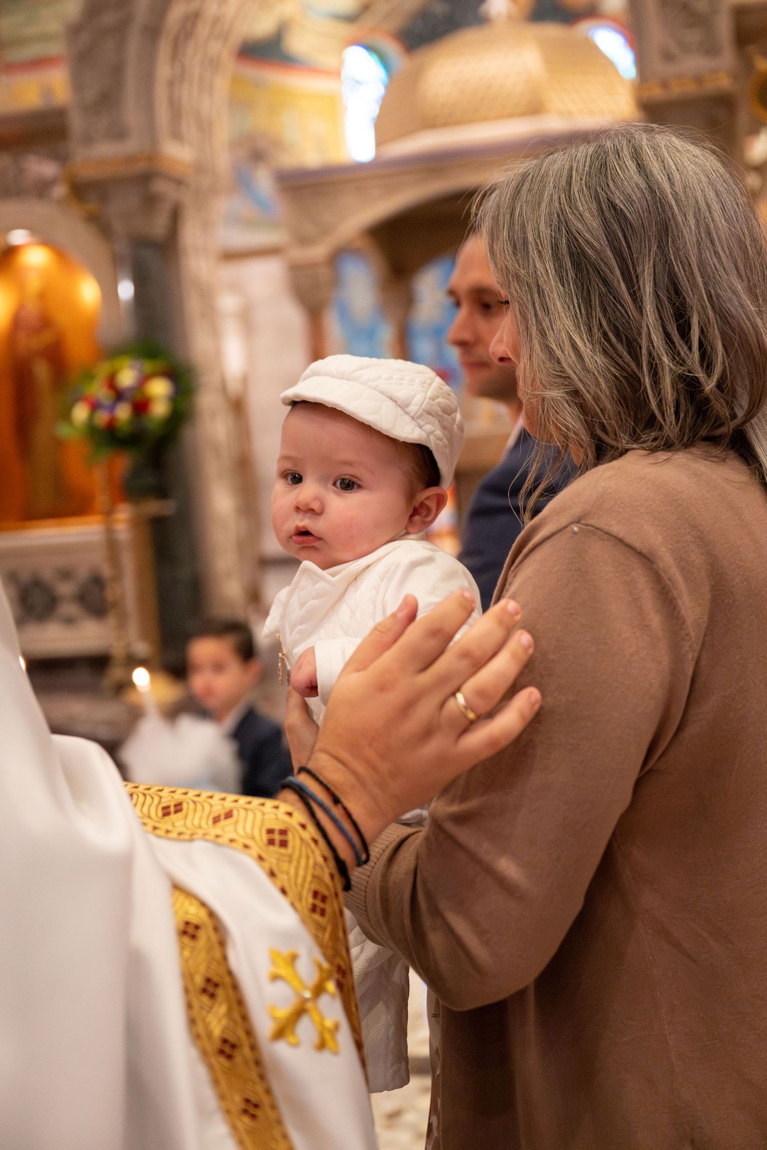A baby in white baptismal attire is held during a traditional church ceremony.