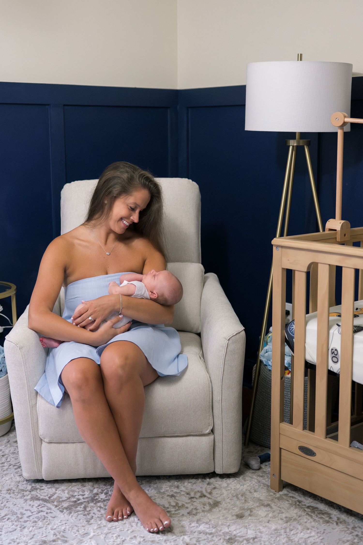 Mother and baby sharing quiet moment in nursery with navy blue walls and beige armchair.