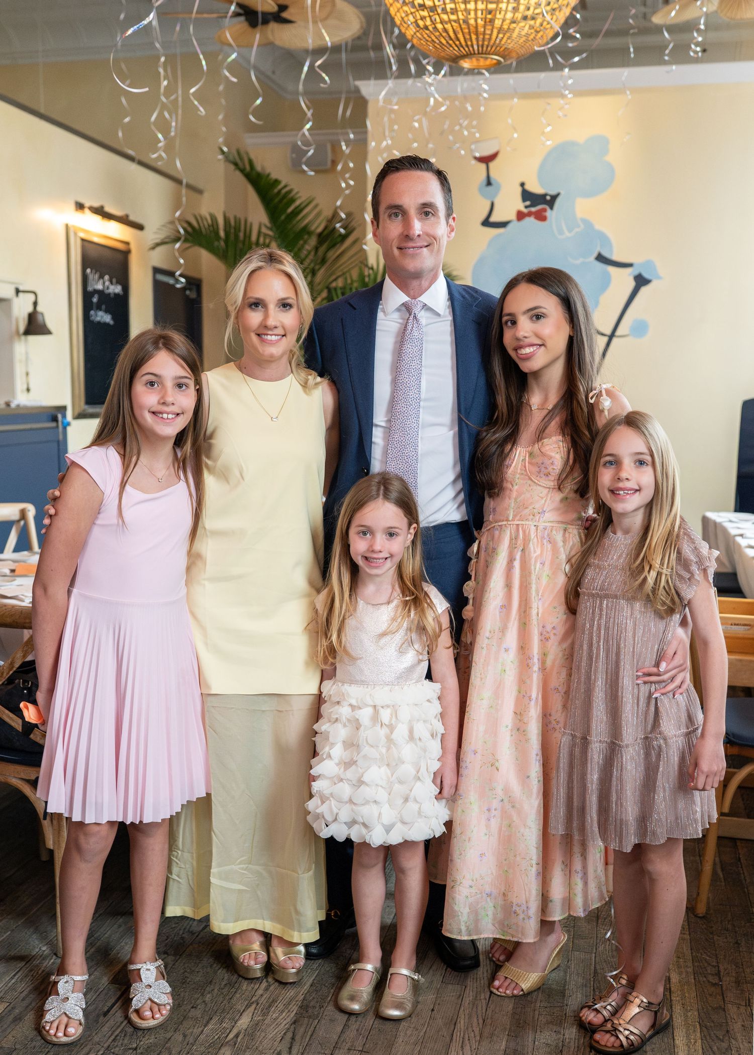 Family portrait with parents and four daughters in pastel dresses at wedding celebration.