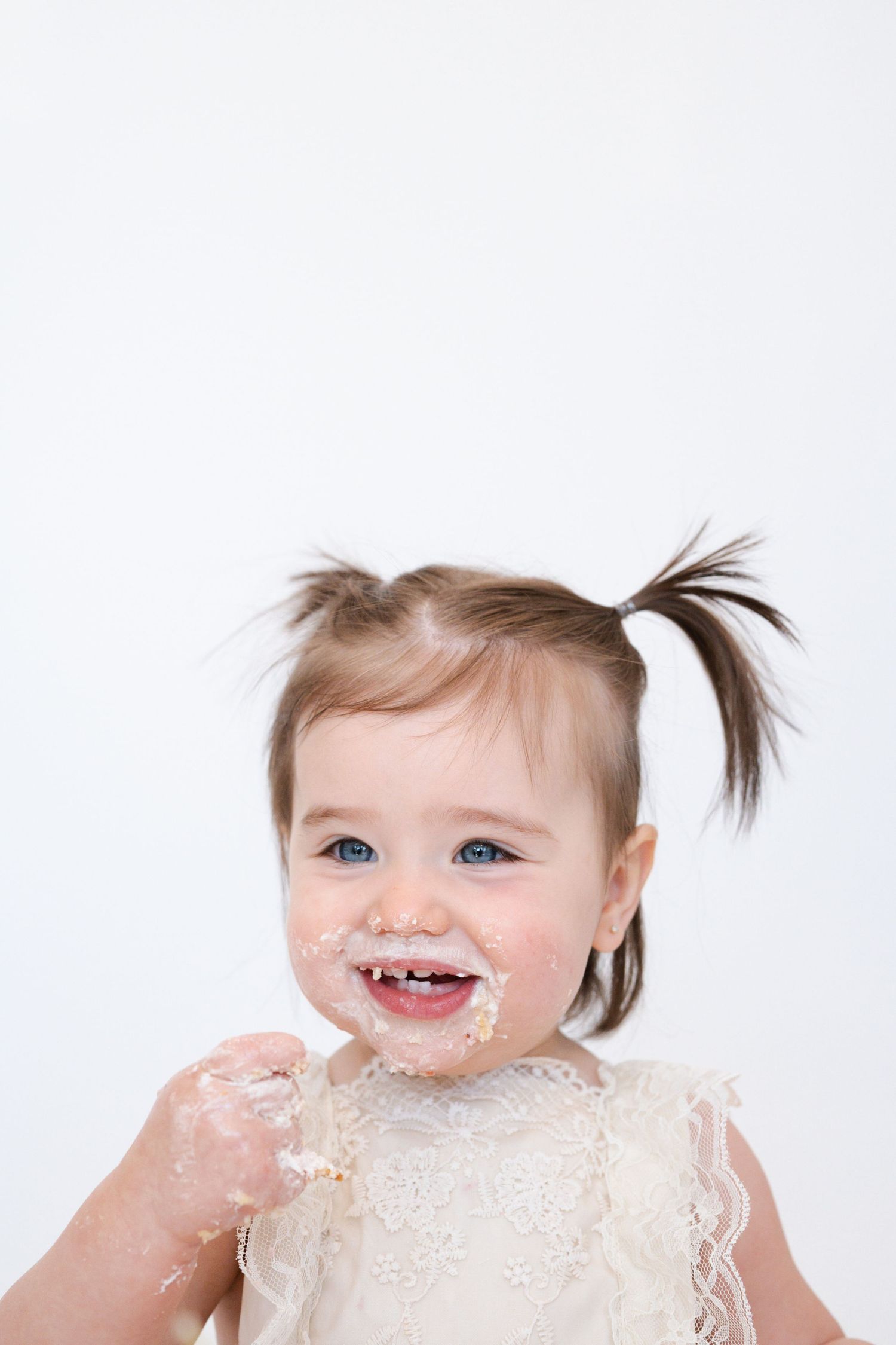Happy toddler wearing cream lace dress with messy face and pigtails.
