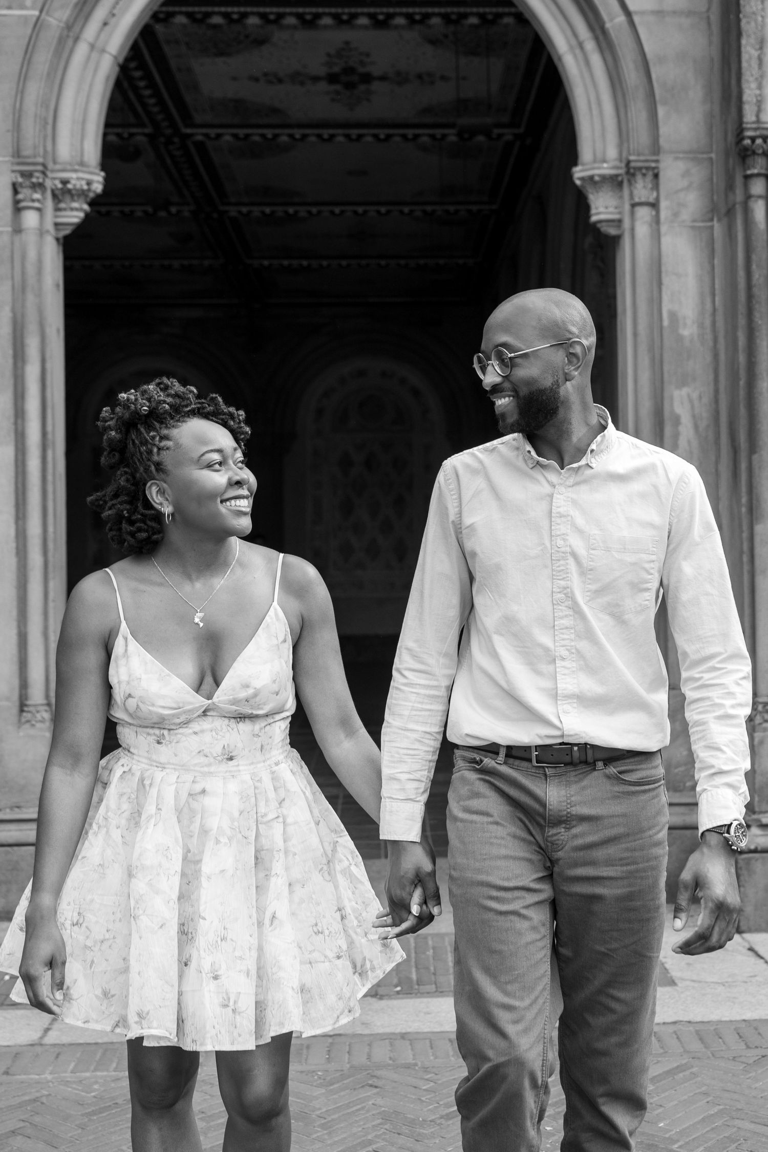 A couple walks together through an ornate archway in coordinated outfits.