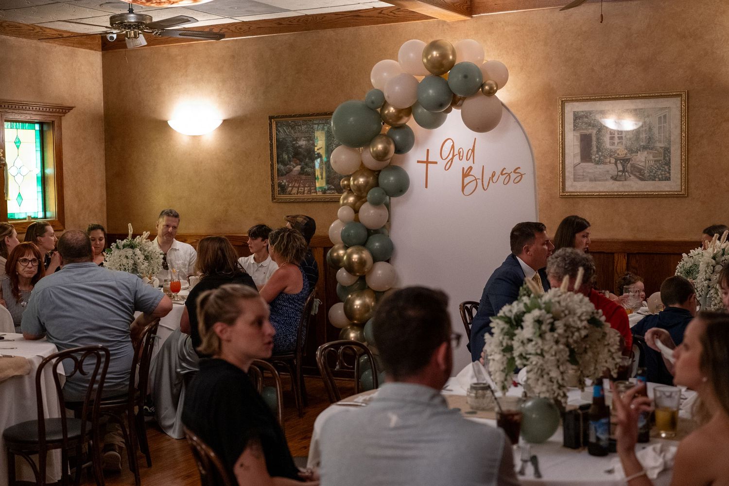 Wedding reception guests gathered in a warmly lit rustic venue with wooden beams and tables decorated with centerpieces.