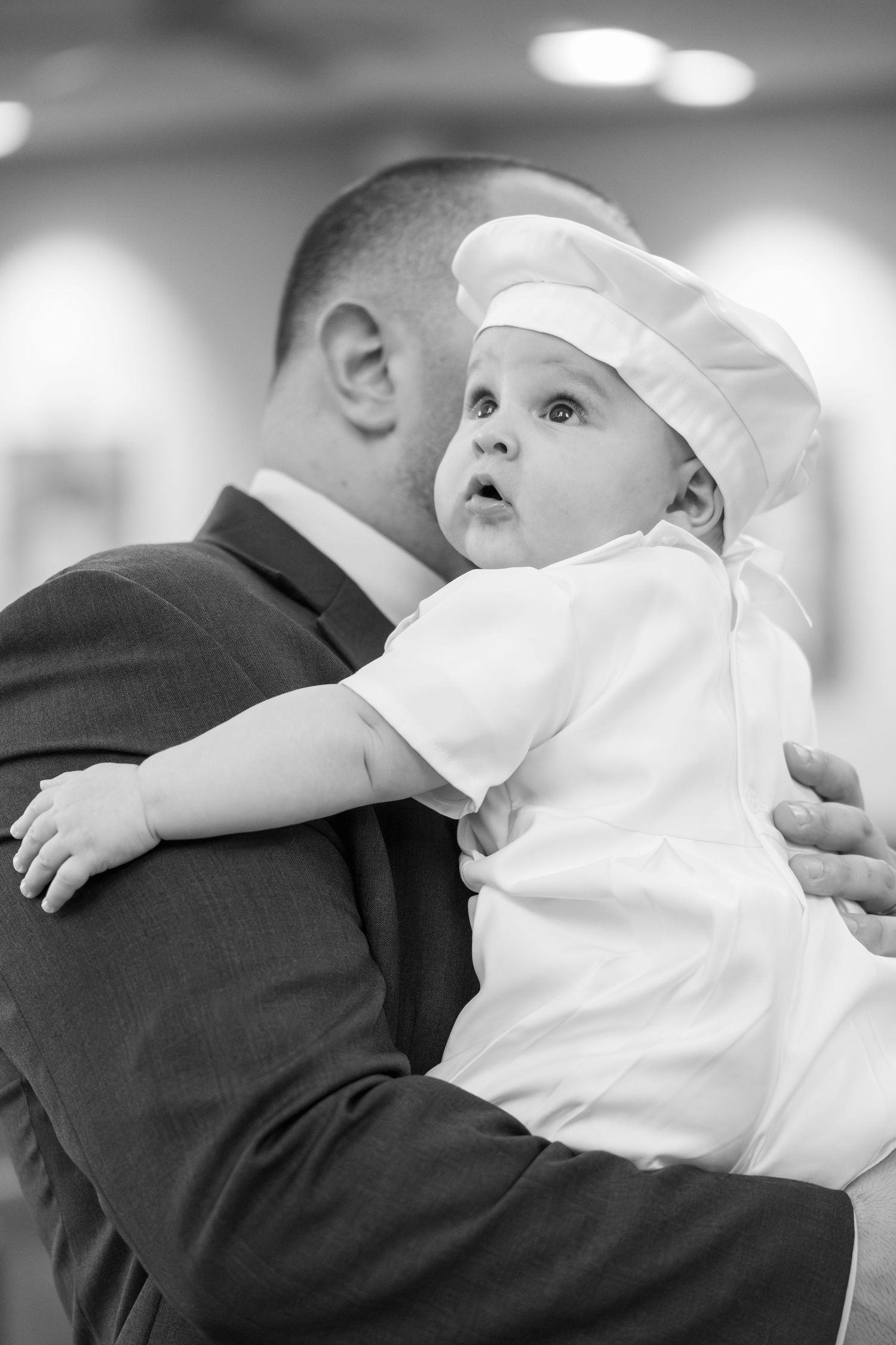 A series of black and white photos showing a baby in white christening gown being held during a baptism ceremony.