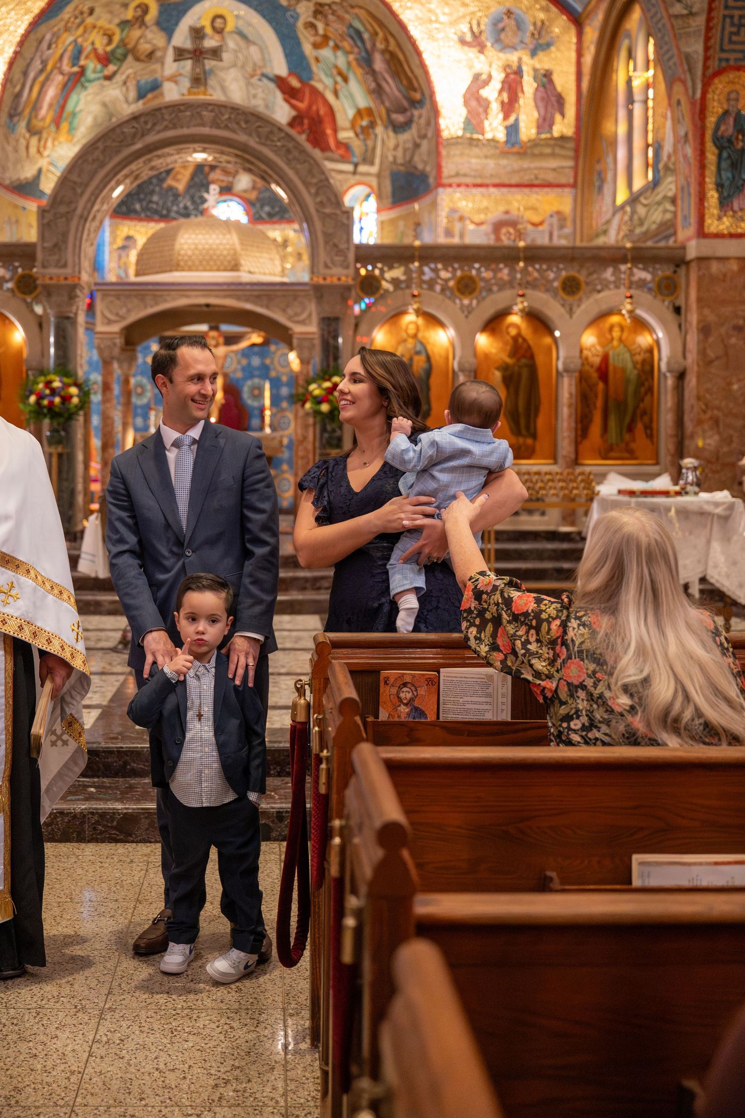 Orthodox church interior with ornate frescoes and wooden pews during baptism ceremony.