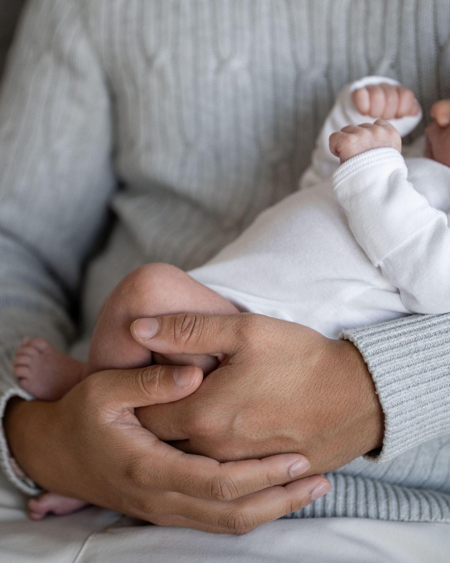 Close-up series of hands gently holding a newborn baby in white clothing.