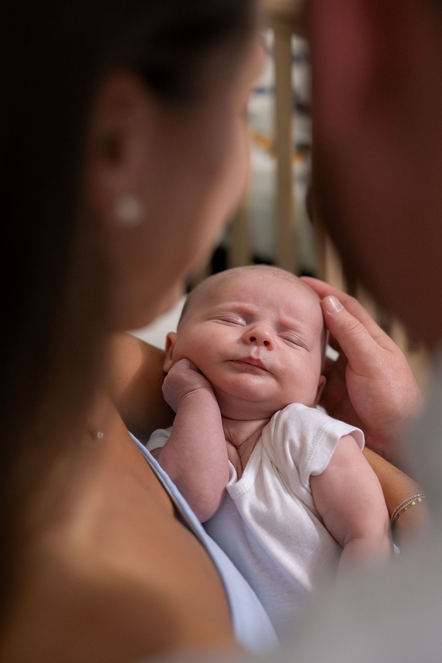 Sleeping newborn in white outfit being tenderly held against soft background.