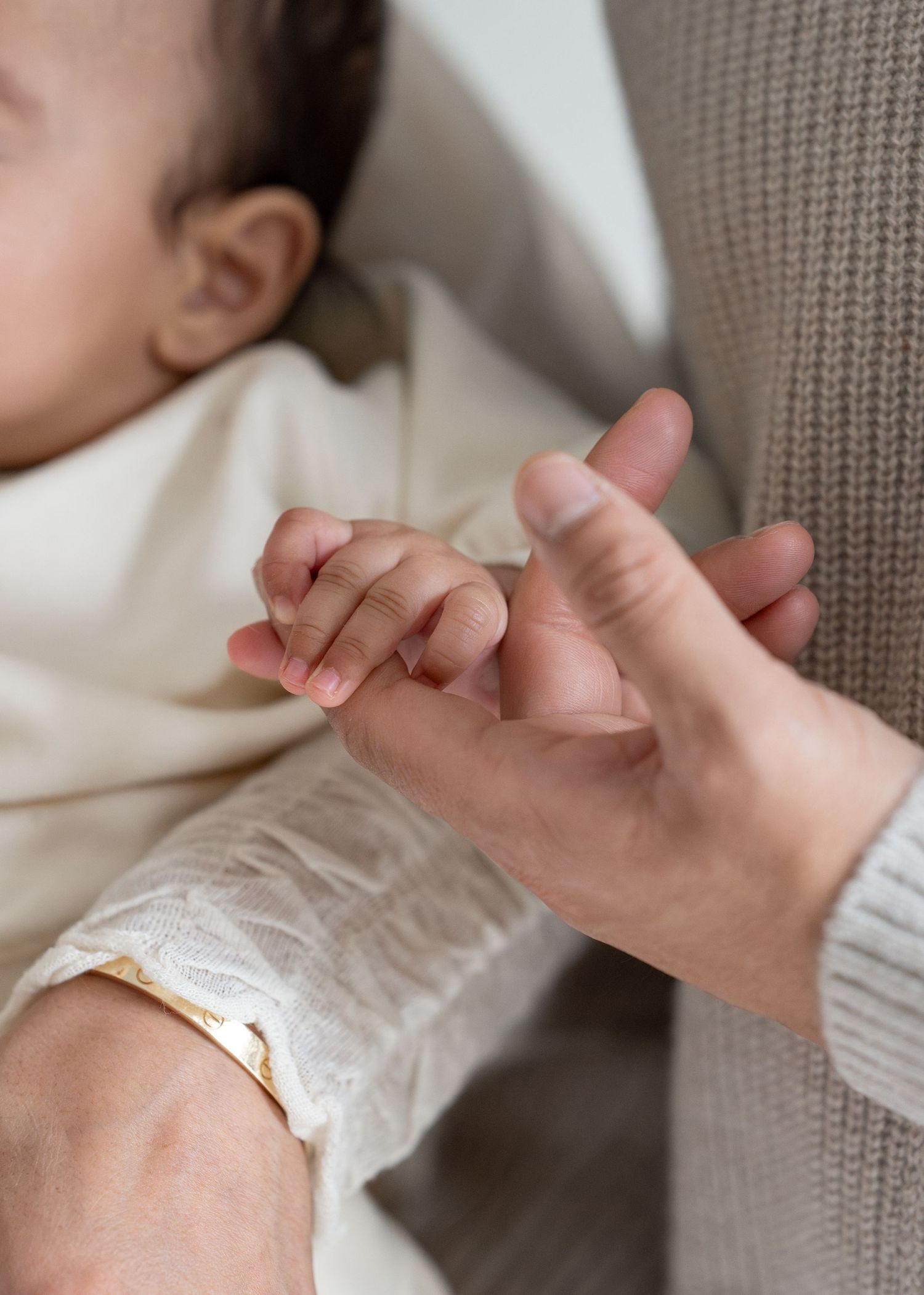 Close-up view of hands holding and examining a delicate gold bracelet against a neutral background.