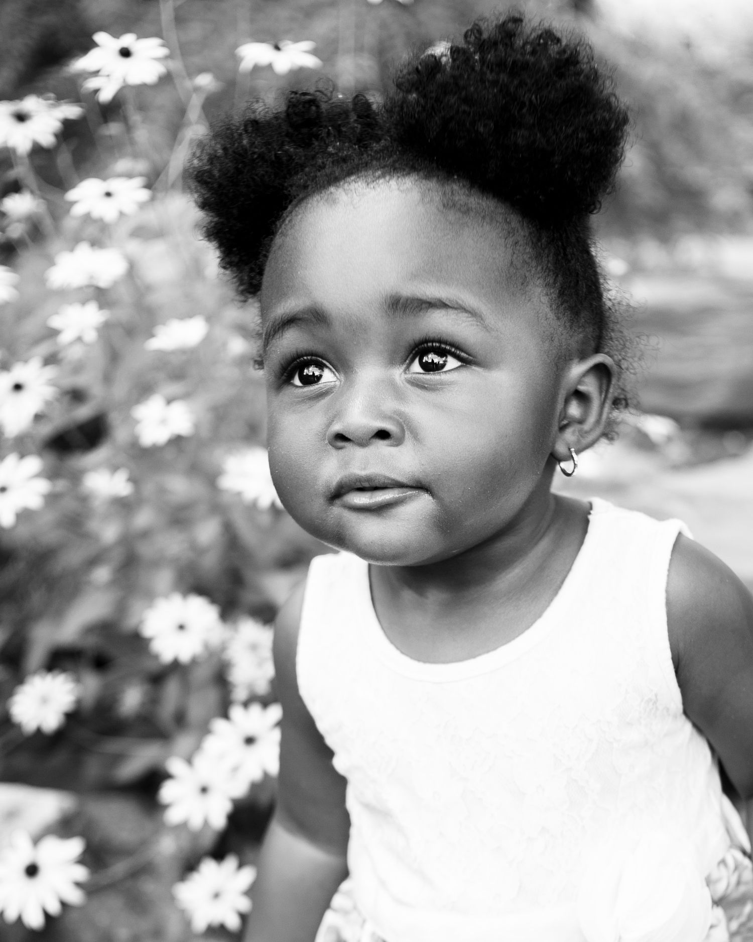 Black and white portrait of smiling toddler with daisies in background.