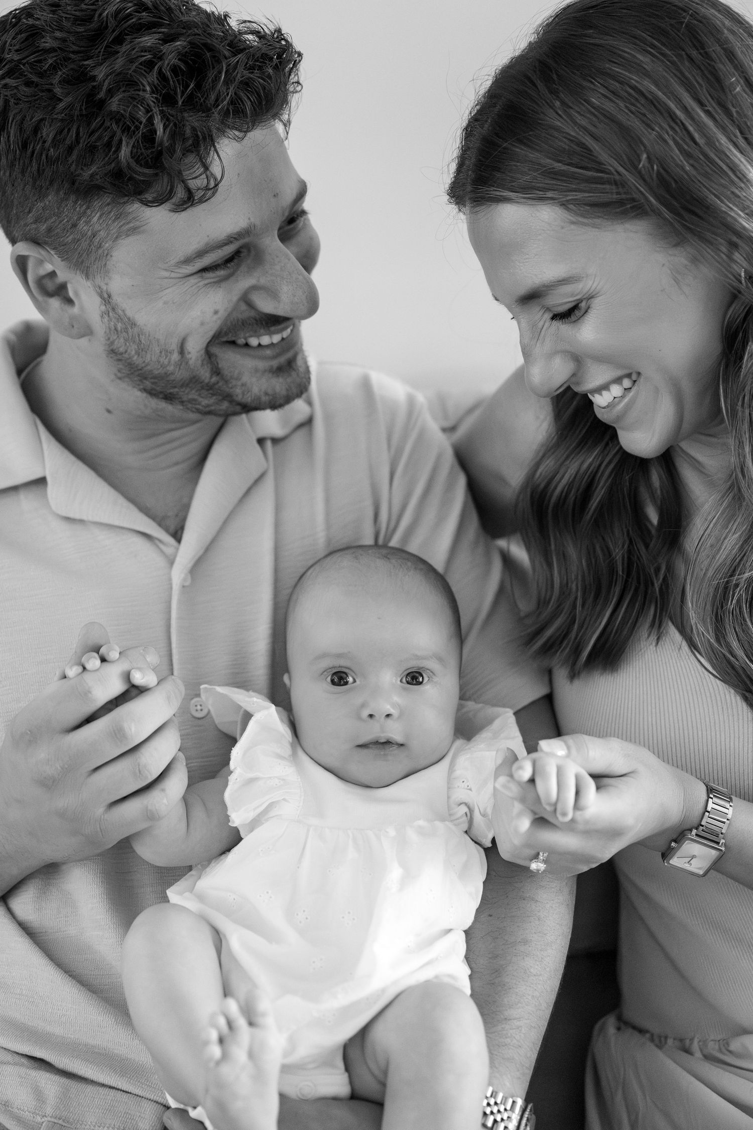Black and white family portrait capturing tender moments with infant in white clothing.