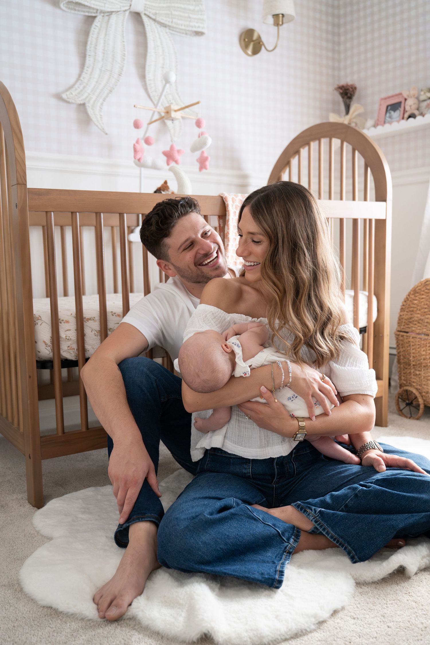 Family sharing playful moments on white carpet in a nursery setting.