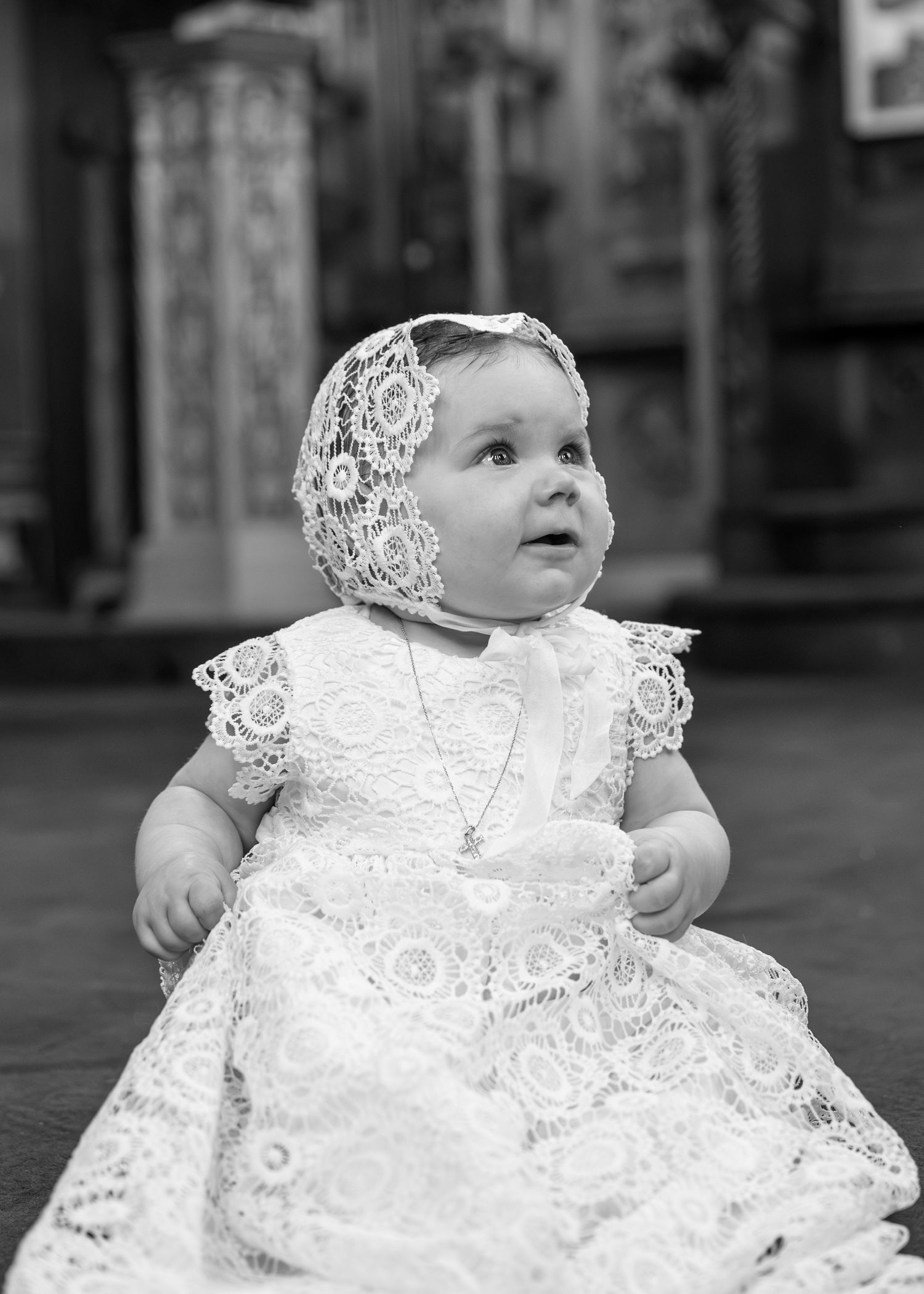 Adorable baby in white lace christening gown and bonnet with cross necklace.