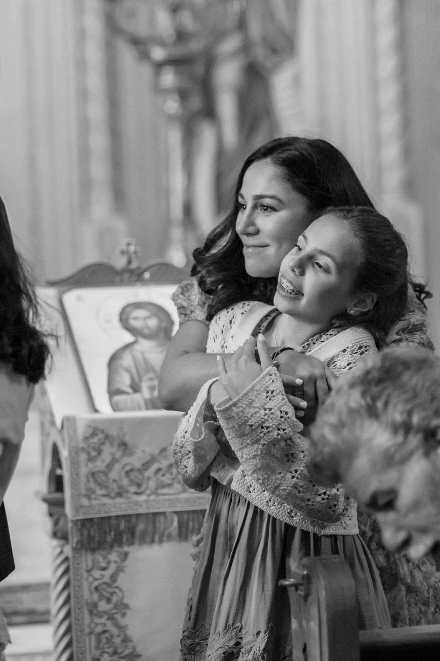 A black and white photograph shows two people in period dress sharing a joyful moment in front of religious artwork.