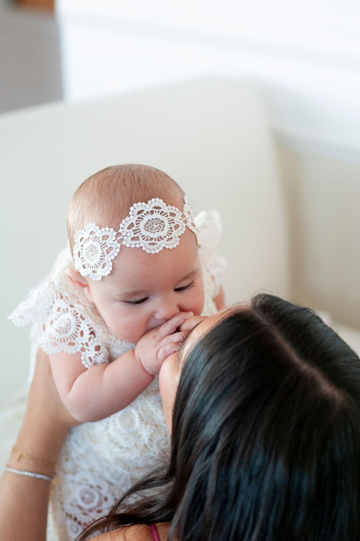 A baby wearing a delicate lace headband rests against someone in an intimate portrait.