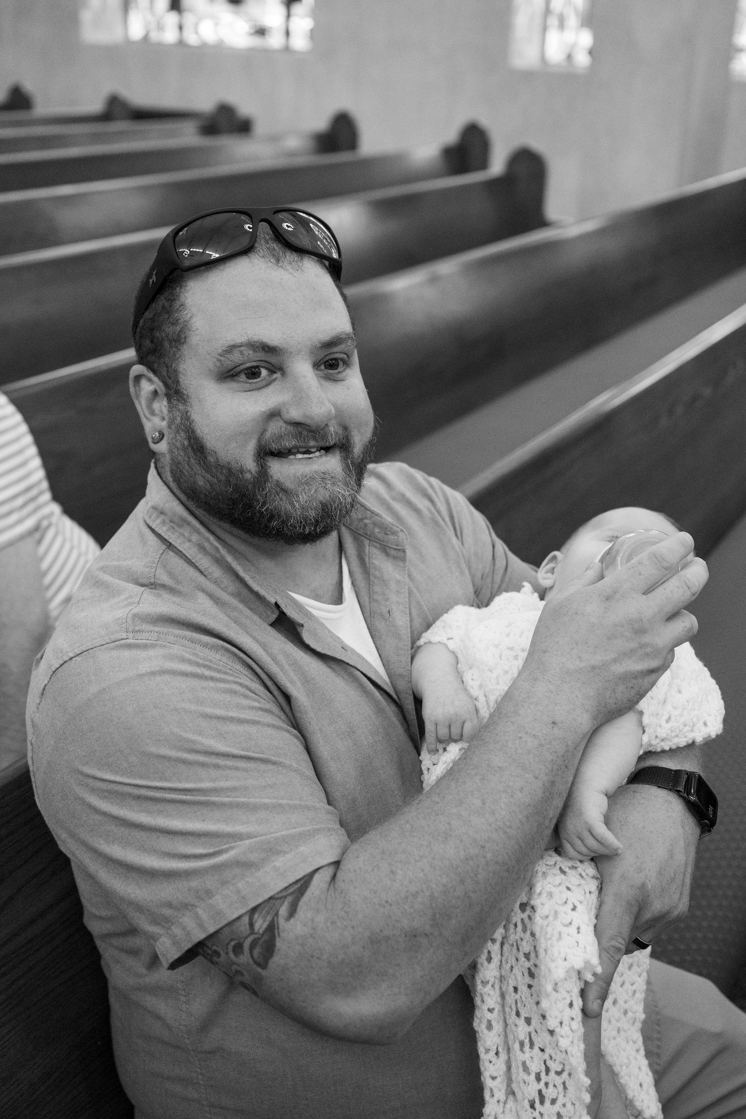 A person in a gray shirt holds a small baby while sitting in a church pew.