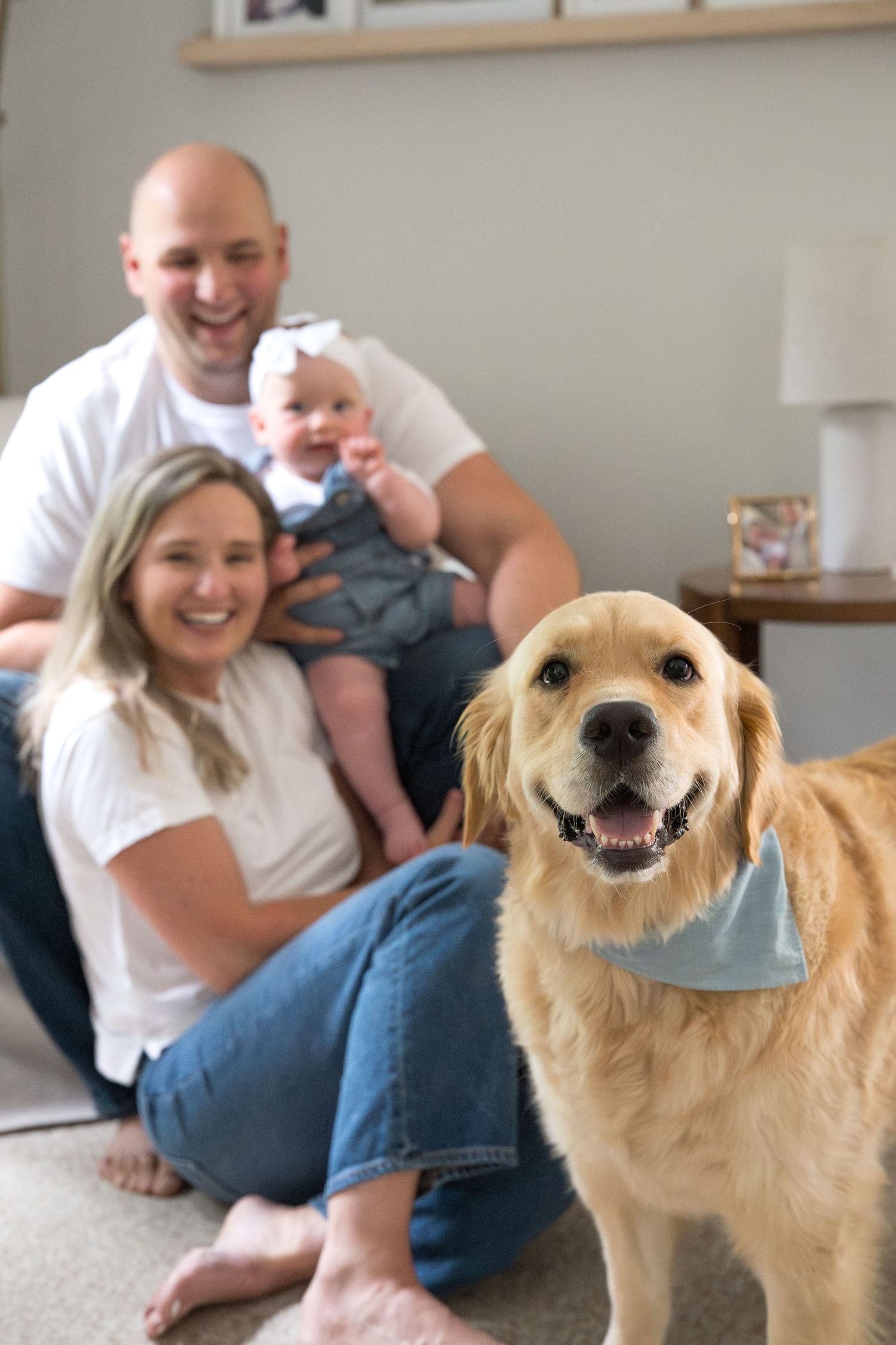 A happy golden retriever smiles alongside family members relaxing on the floor in a bright living room.