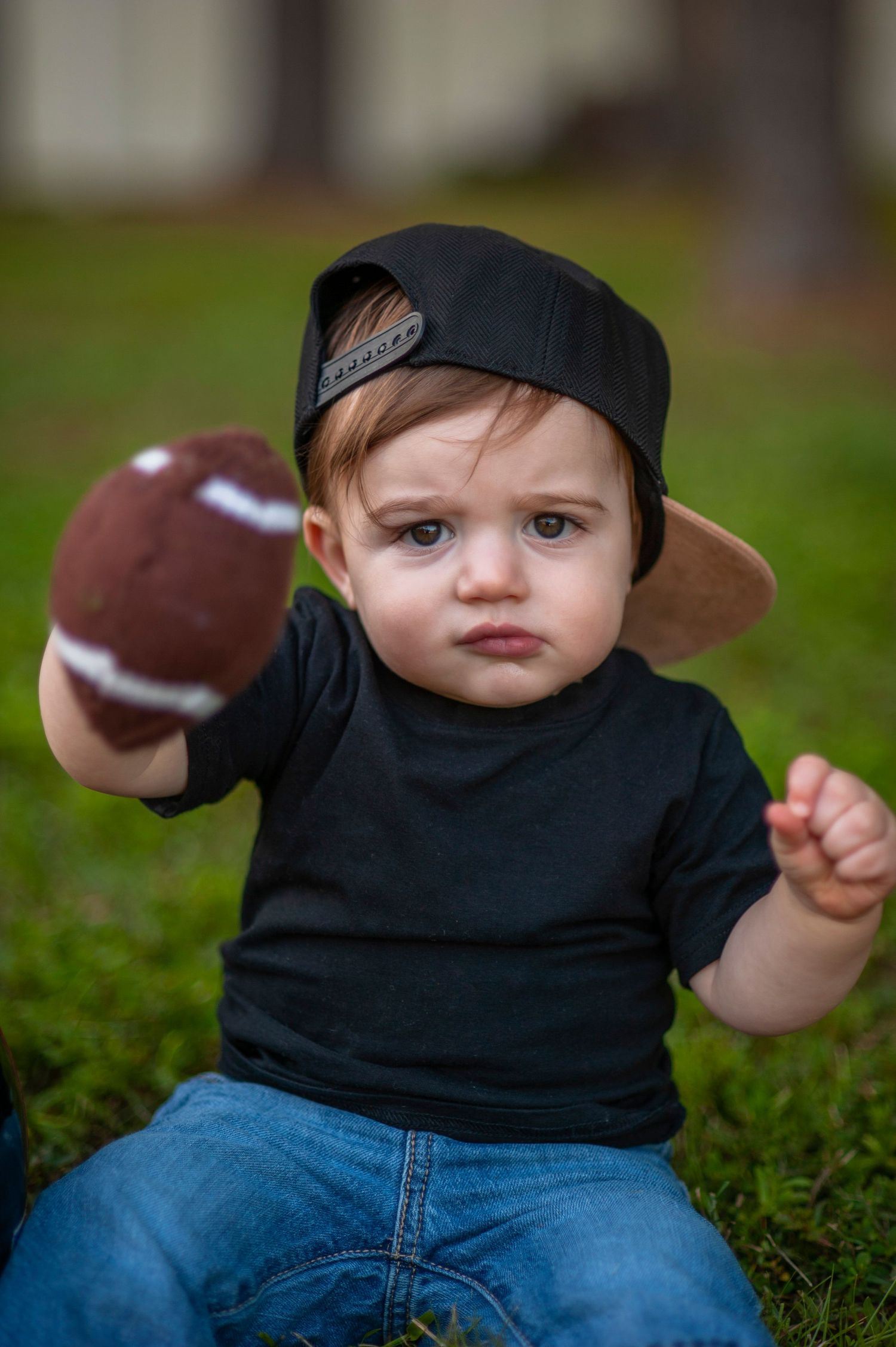 Baby in black shirt and jeans playing with a football on grass.