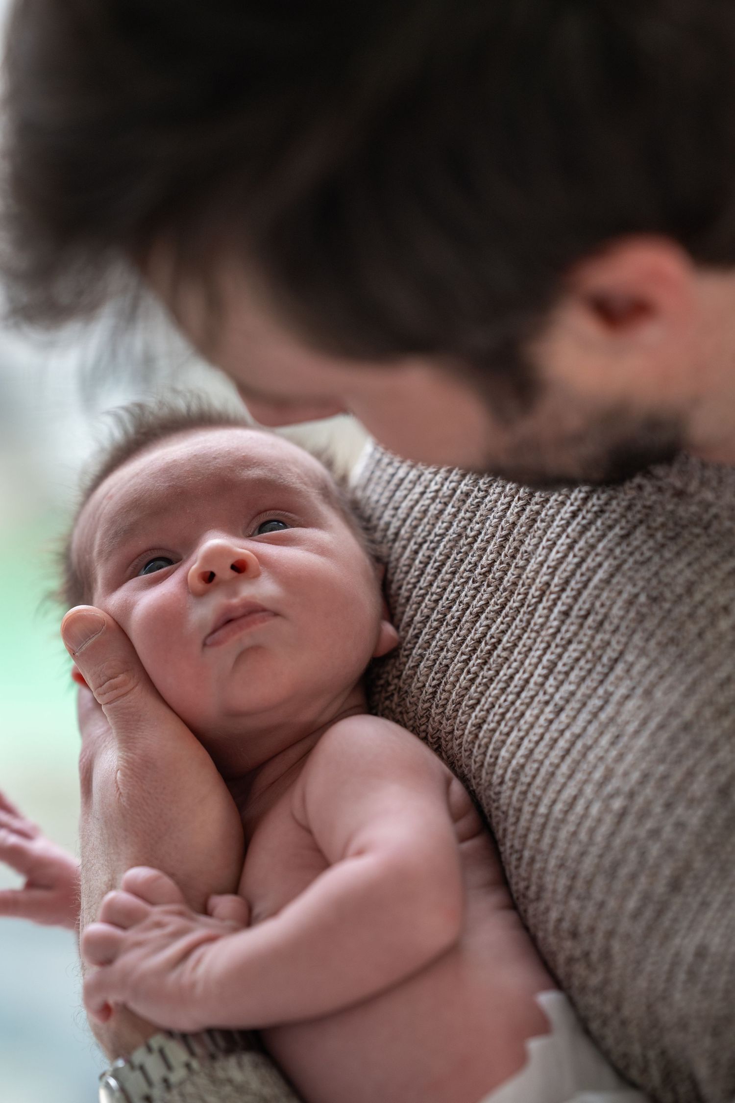 A newborn baby smiles while being cradled in a gray knit sweater.