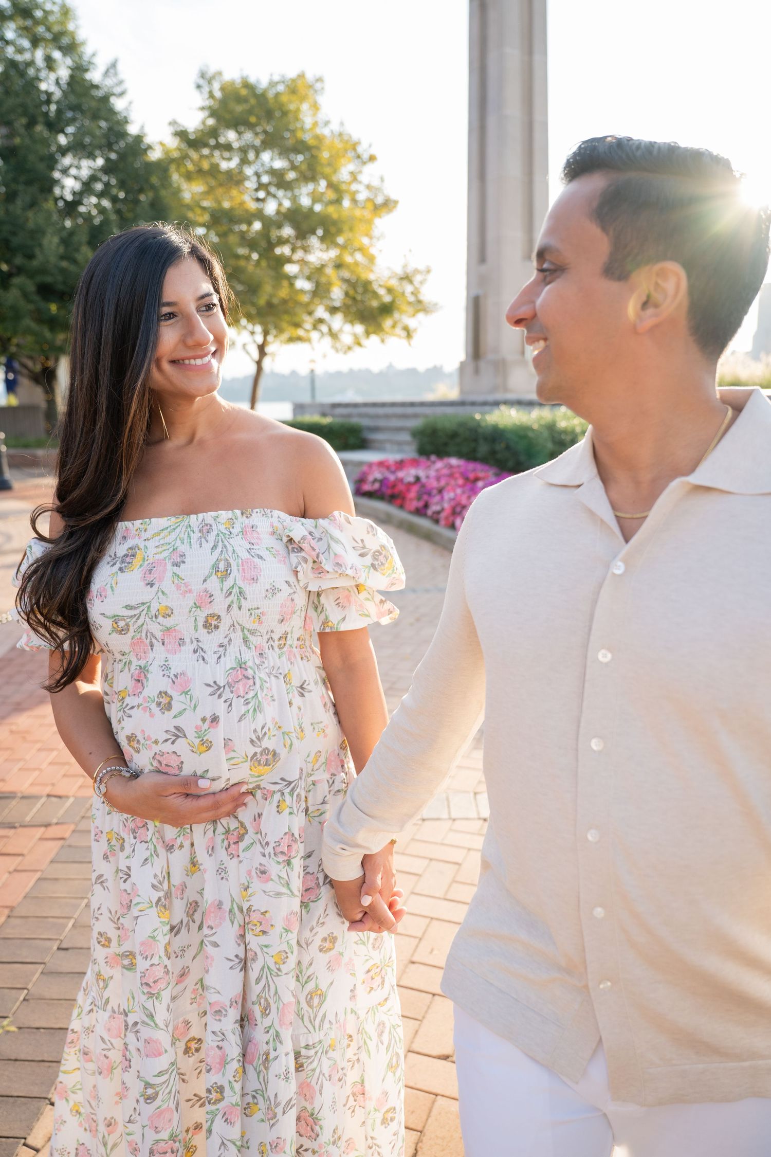 Couple in floral dress and white shirt dancing on outdoor terrace at sunset.