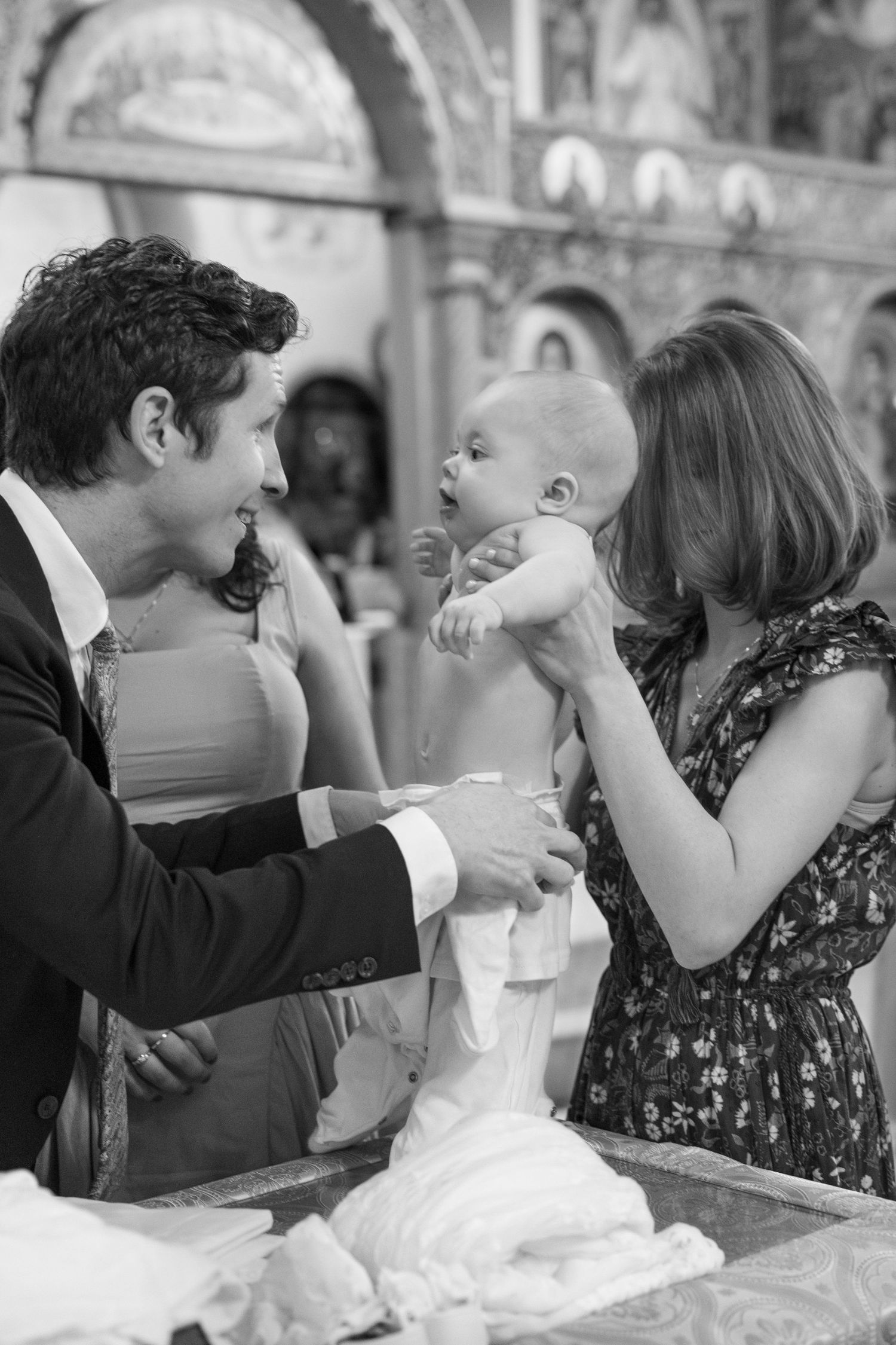 A tender black and white moment between parents and their baby during what appears to be a baptism ceremony.