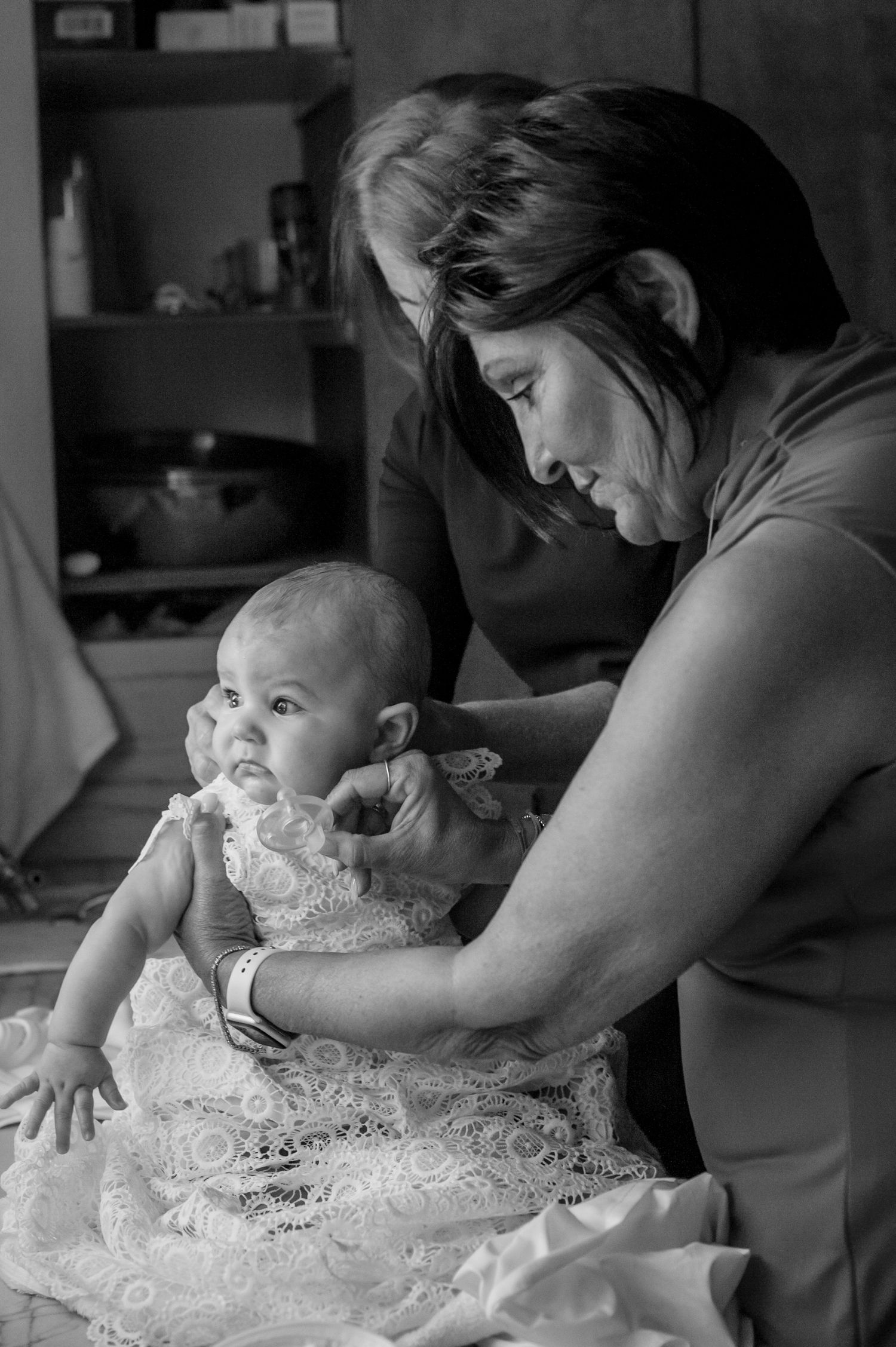 A baby wearing an intricate white lace dress is being dressed and prepared for a special occasion.