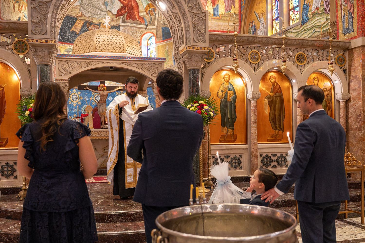 An ornate Orthodox church interior with gilded icons and frescoes during a religious ceremony.