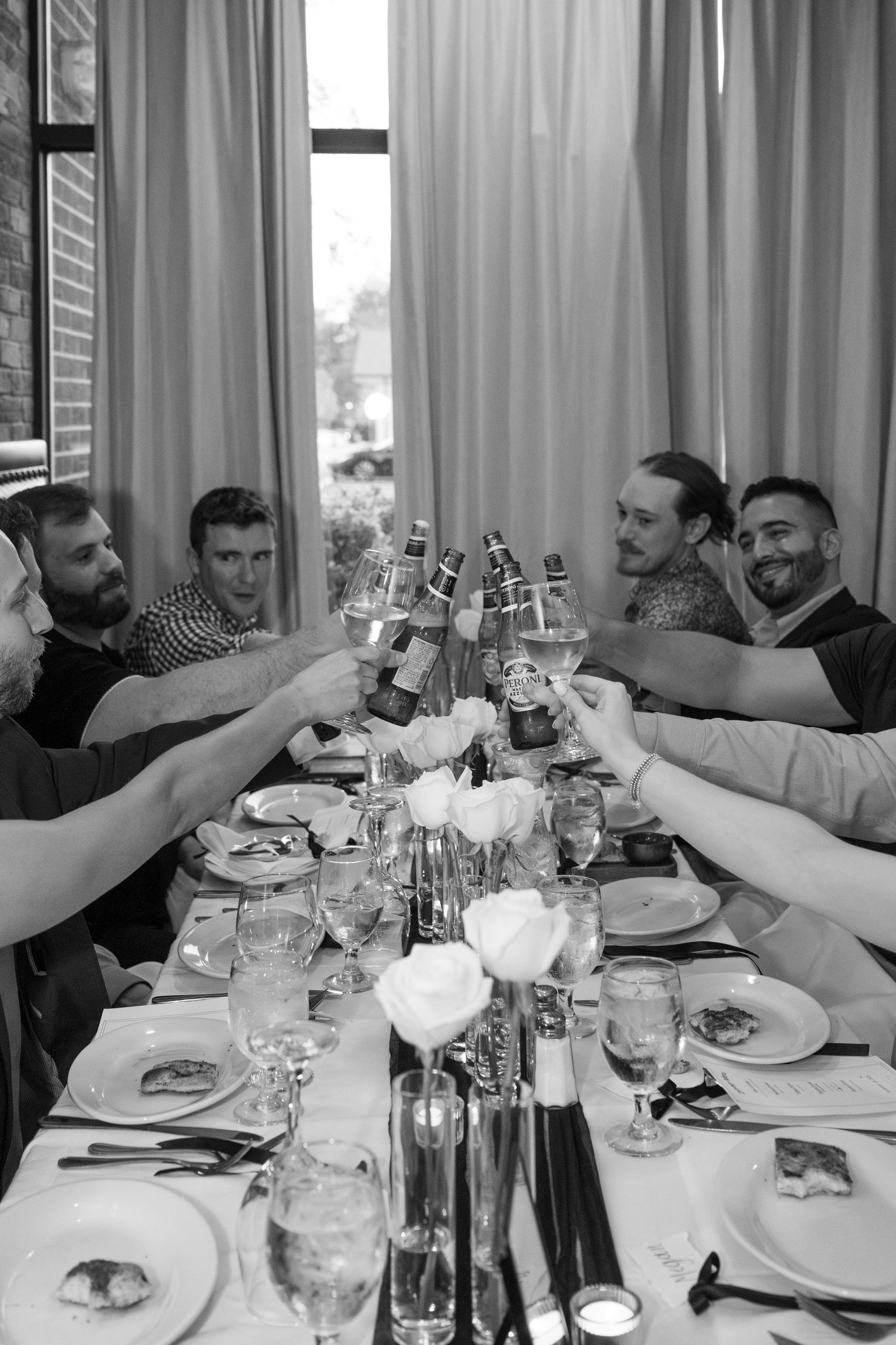 A black and white photo of a group toasting with glasses around a dining table during a celebration.