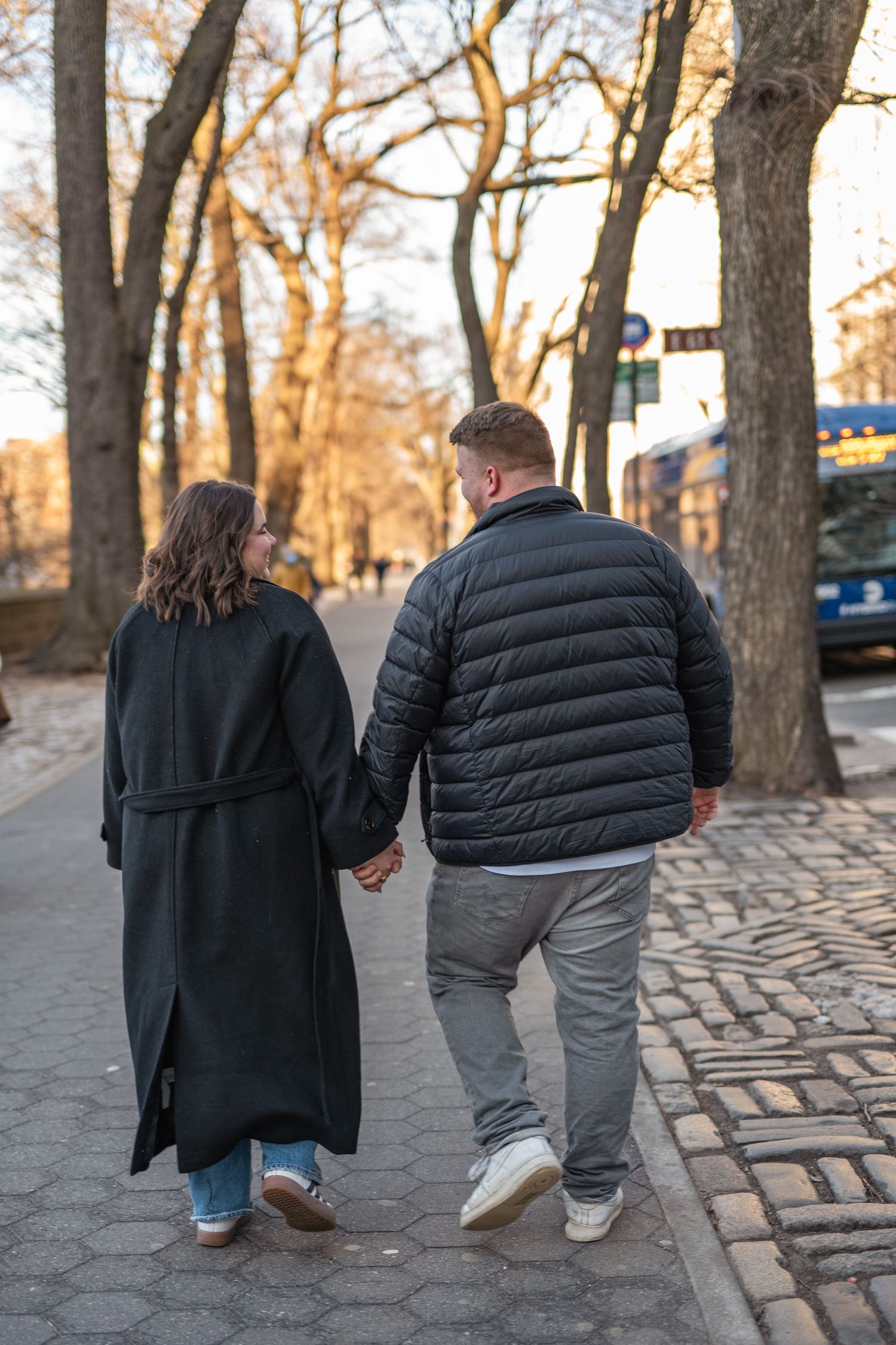 A couple walks hand in hand up stone steps in an autumn park during sunset.