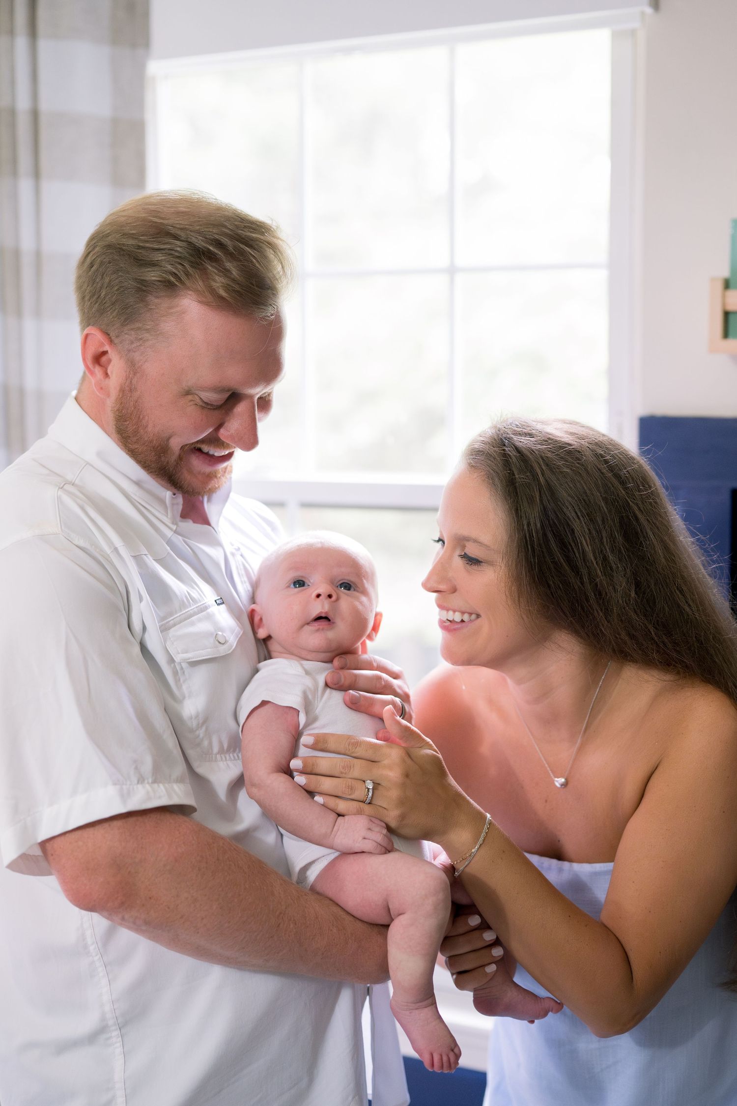Intimate family moment with parents and baby sharing joyful expressions in bright room.
