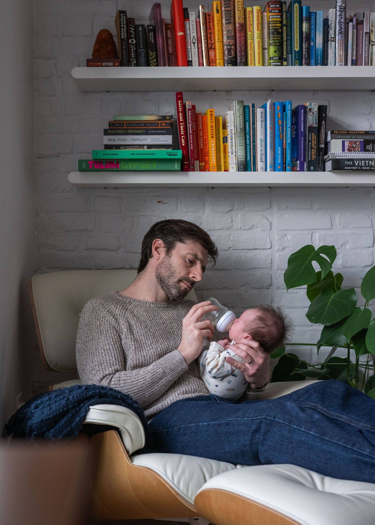 Intimate family moment captured on a couch beneath white floating bookshelves.