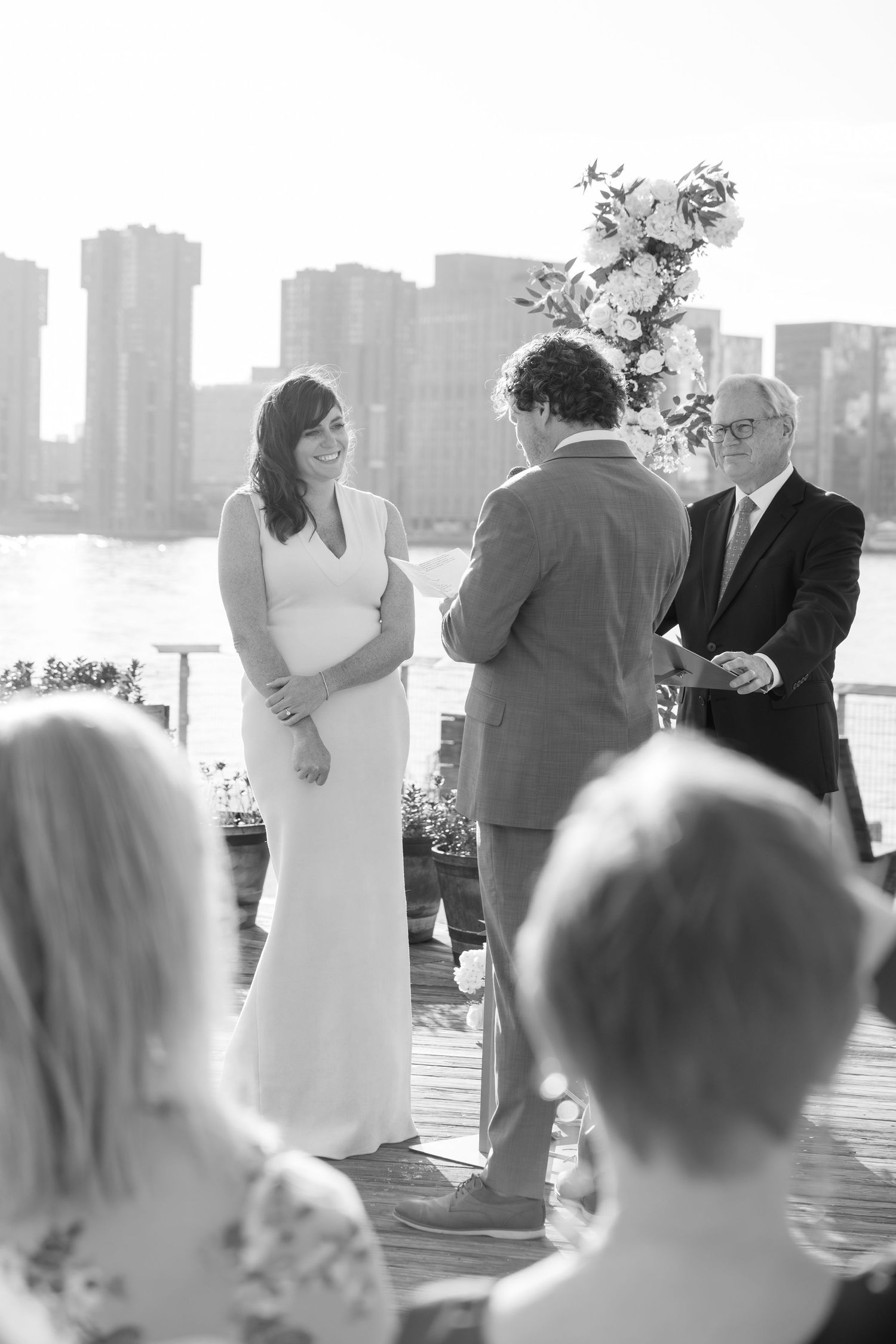 Wedding ceremony taking place on a waterfront with city skyline in background.