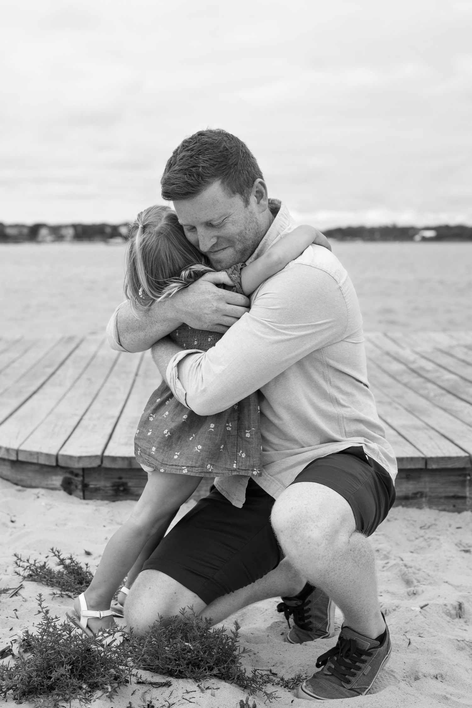 Intimate black and white photos of a couple embracing on a wooden dock by the water.