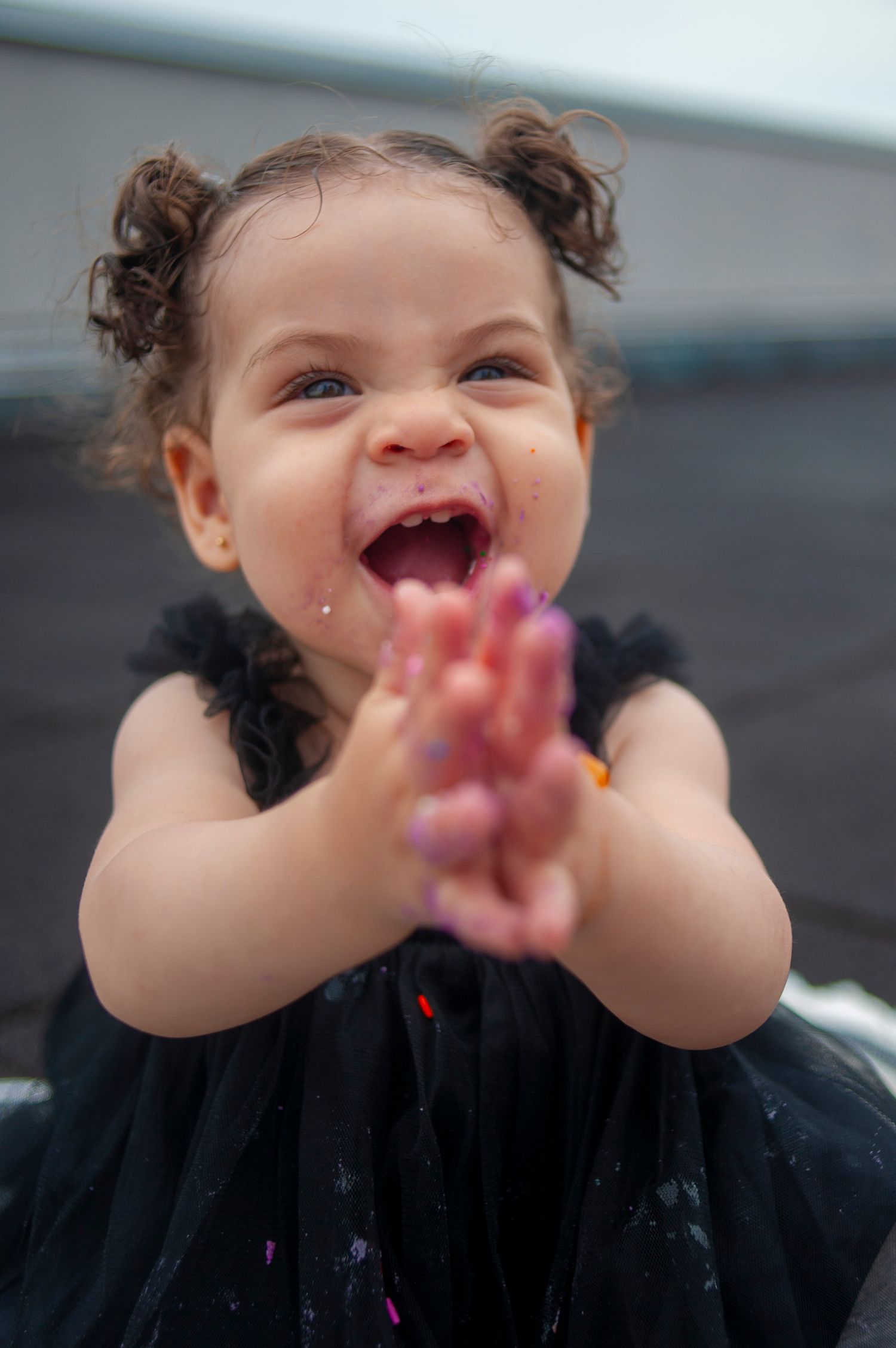 Young child in black dress clapping hands with joyful expression.