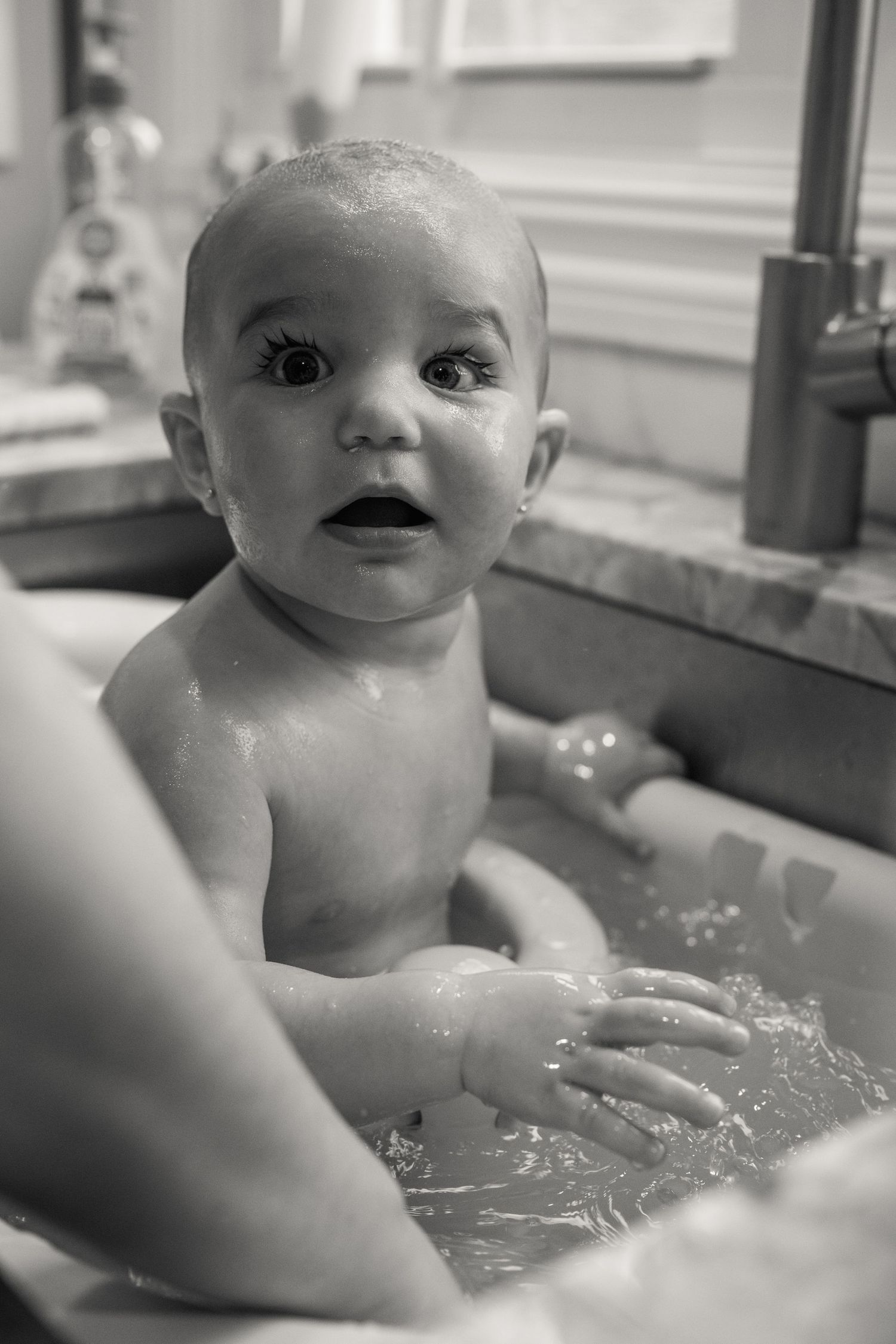A baby enjoys bathtime with water splashing in black and white photographs.