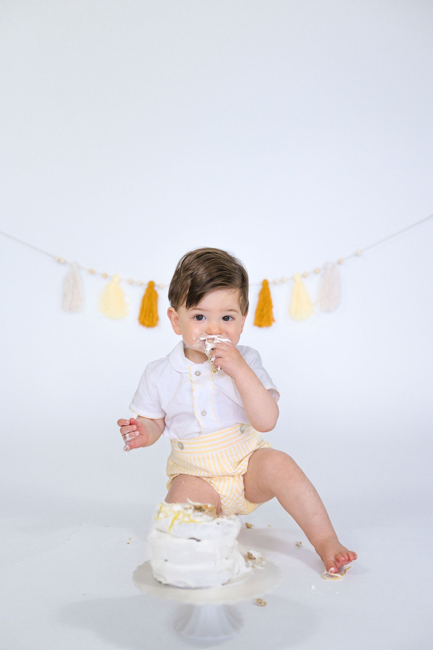 Baby tastes frosting from birthday cake during festive photo session.